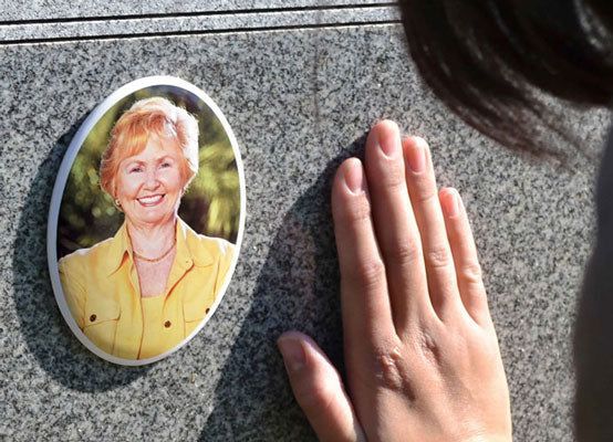 A person is touching a gravestone with a ceramic picture of a woman