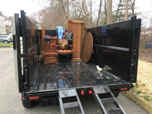 A truck bed loaded with furniture. Includes a wooden cabinet, chairs, and table.
