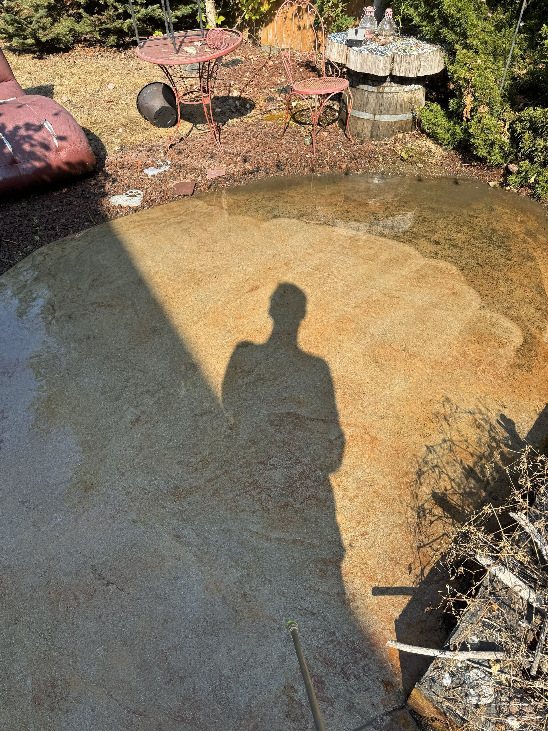 Shadow of person on sunny patio with brown and wet patches.
