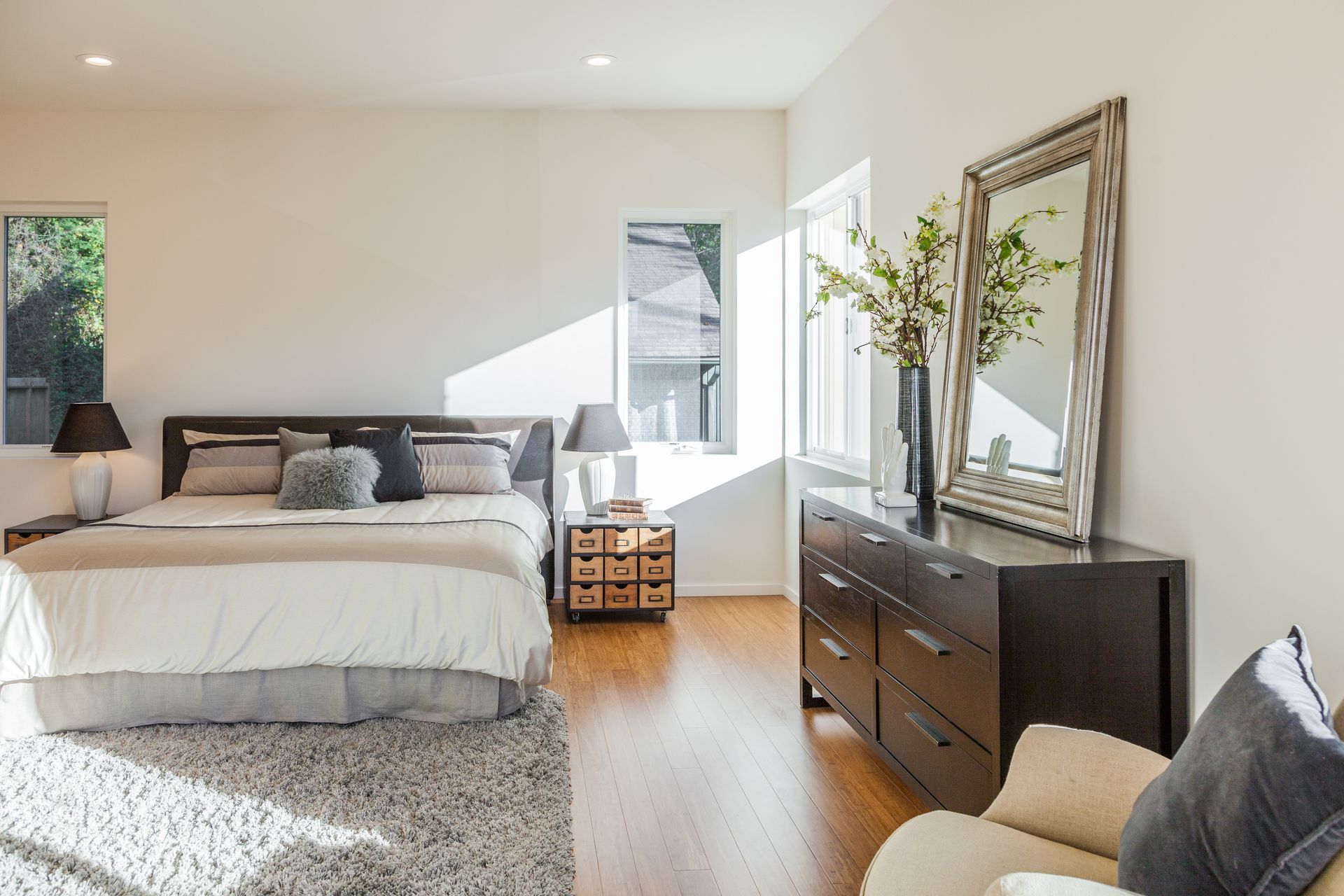 Bedroom with king-sized bed, dresser, and large mirror. Sunlight streams through windows.