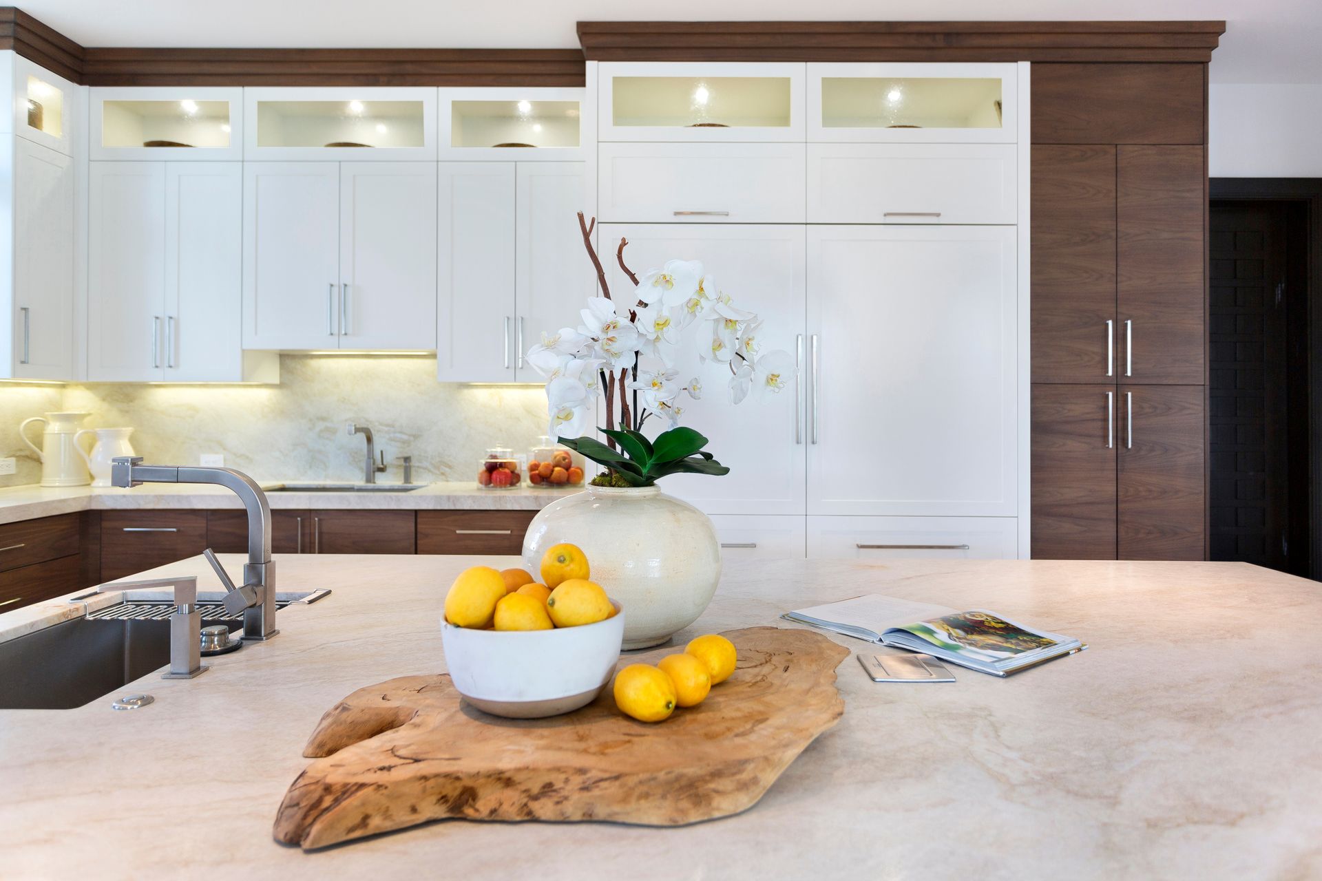 Modern kitchen with white and brown cabinets, large island with wooden slab, orchids, and lemons.