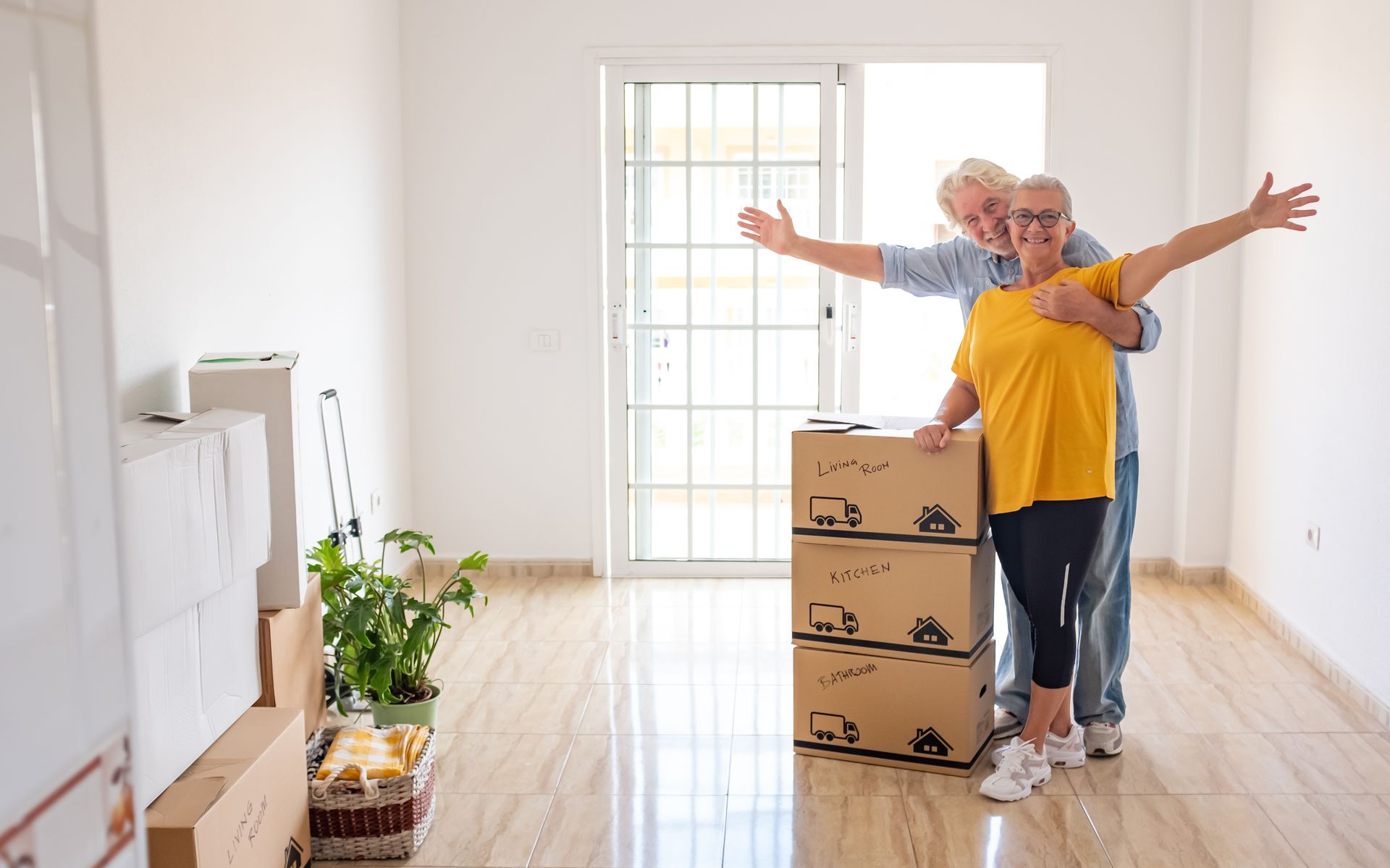 Couple celebrating in a new, empty room with moving boxes, arms outstretched.