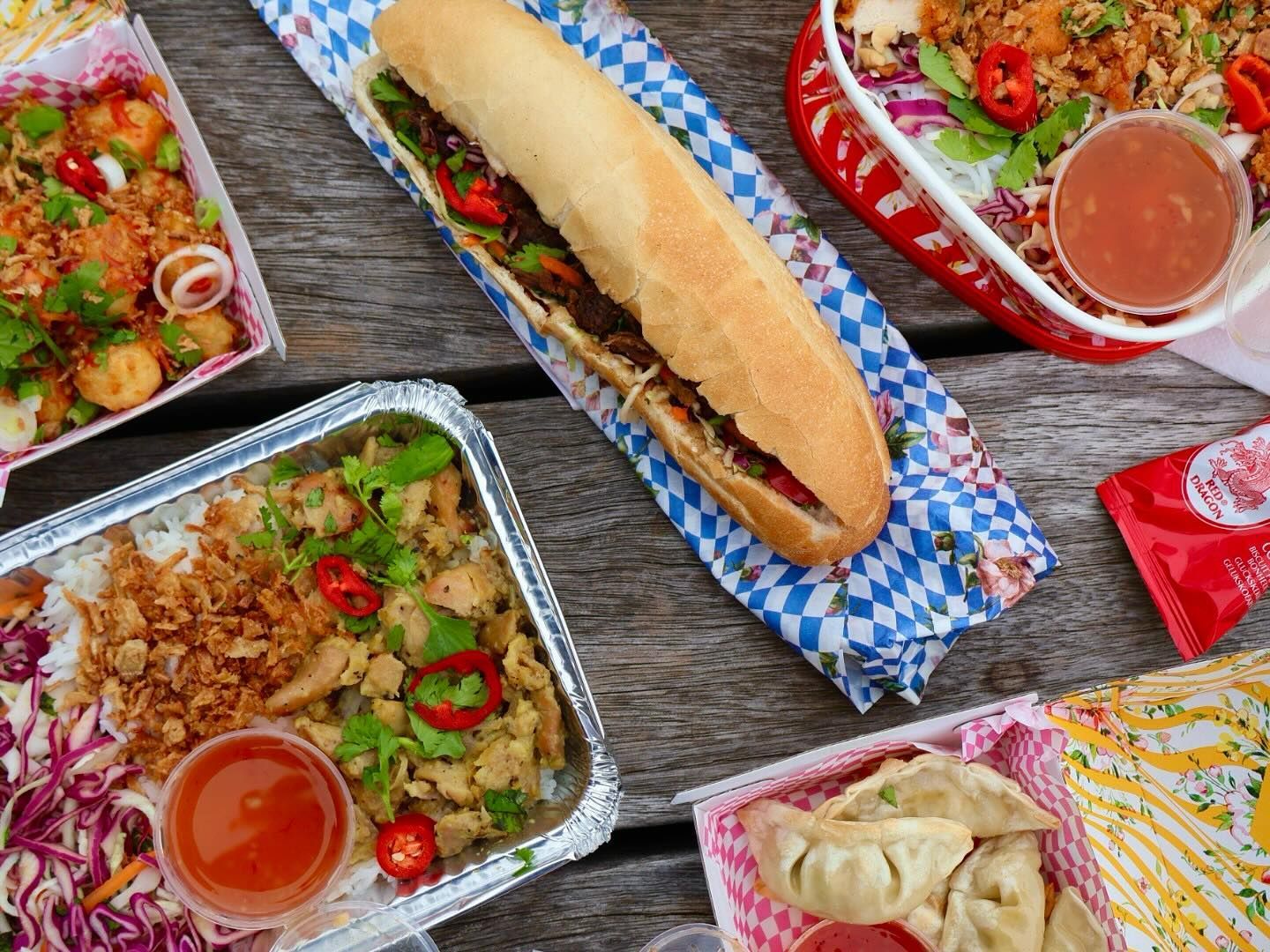 Vietnamese street food from Hop in London with banh mi, dumplings, rice boxes and sauces on wooden table.