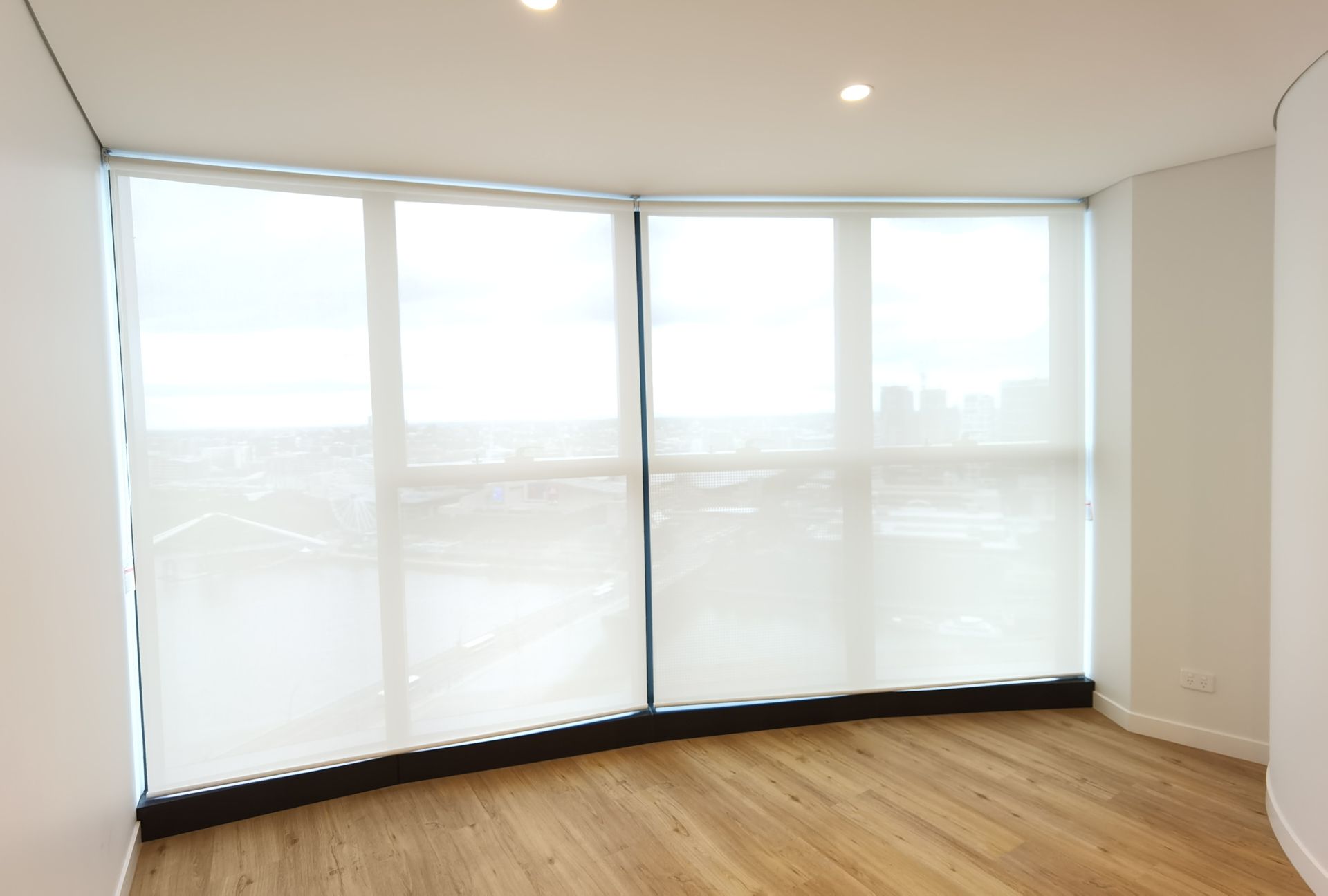 An empty room with a large window and white blinds.