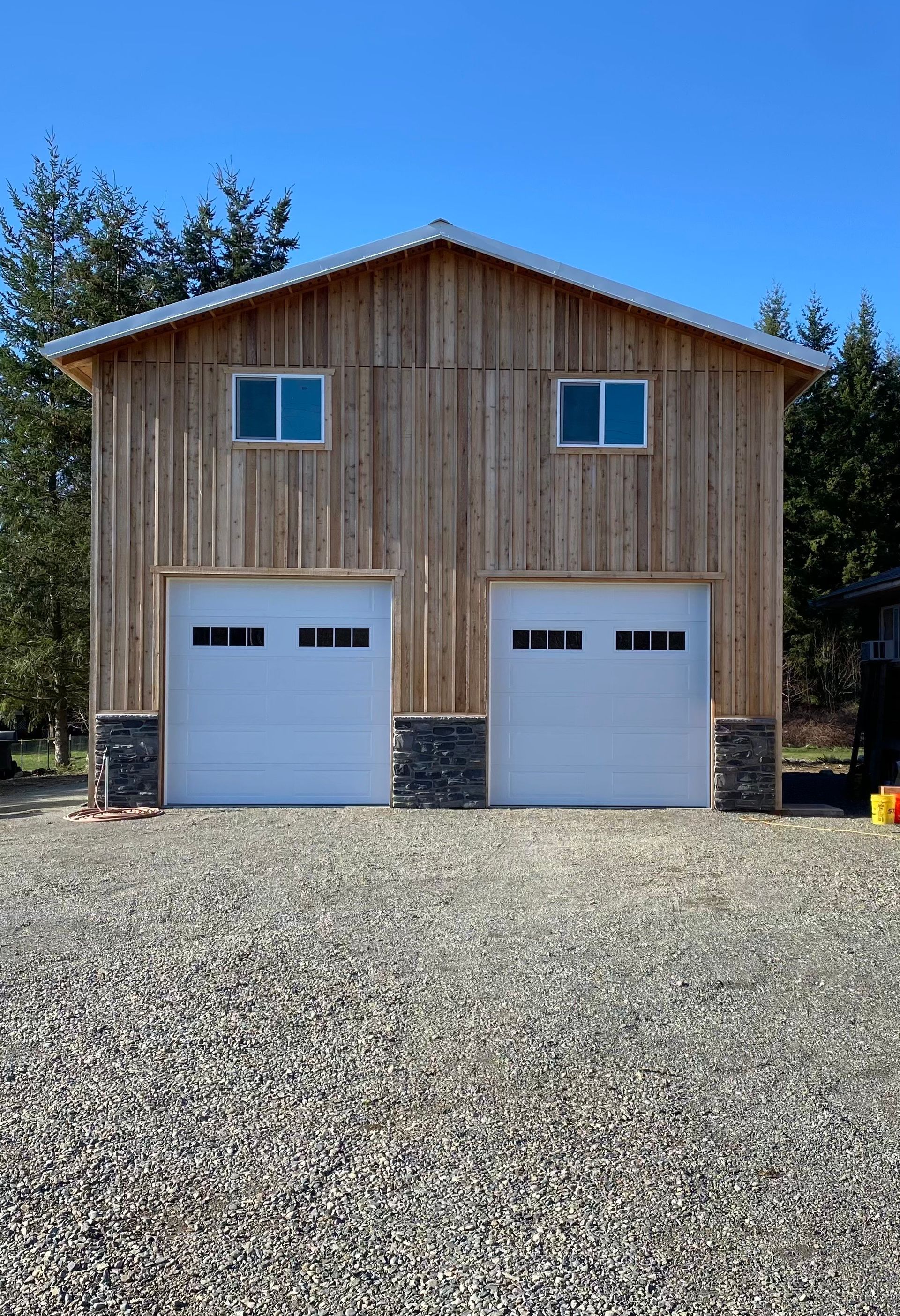 Two-story wooden building with garage doors, windows, and gravel driveway under a blue sky.
