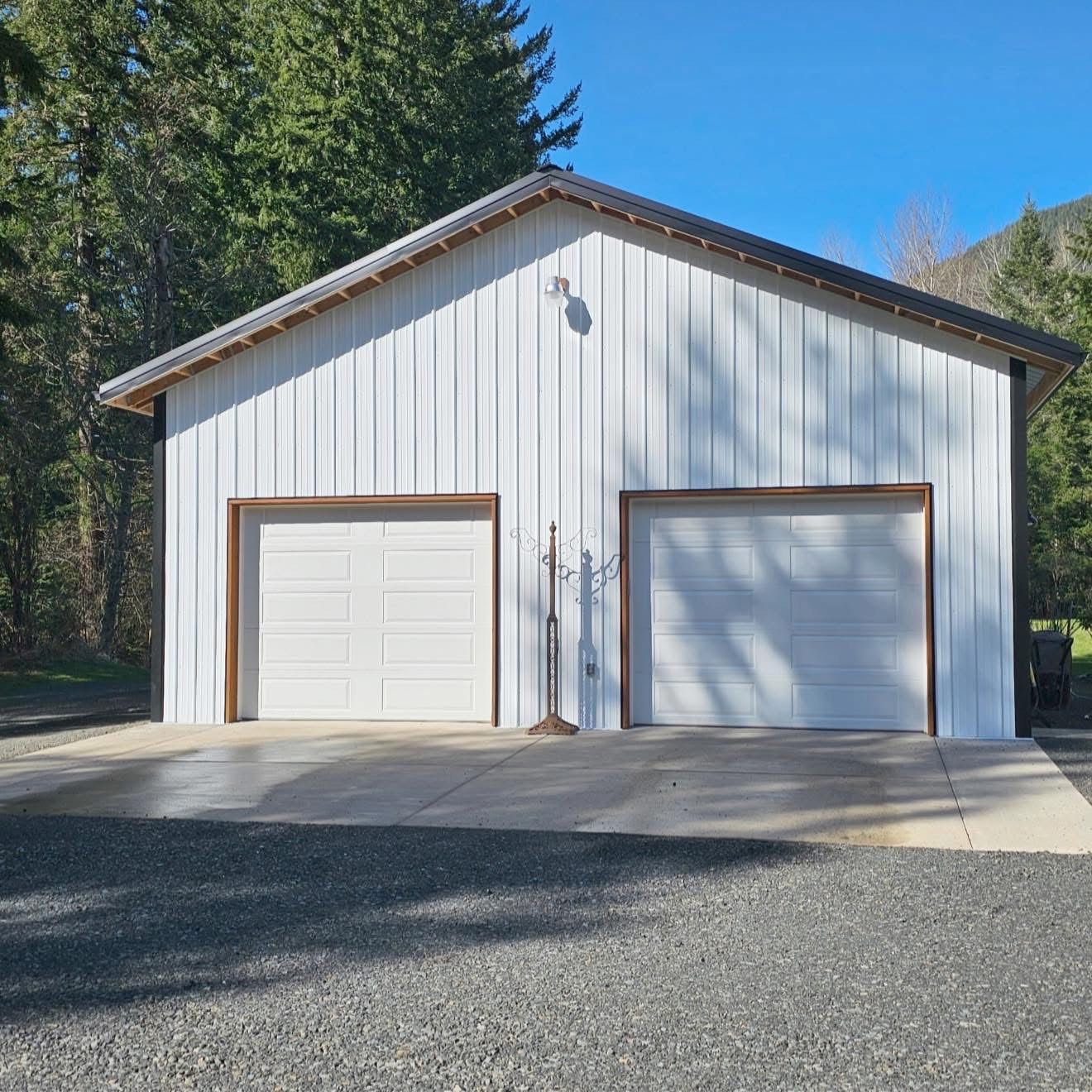 White metal garage with two doors, gravel driveway, and a blue sky.