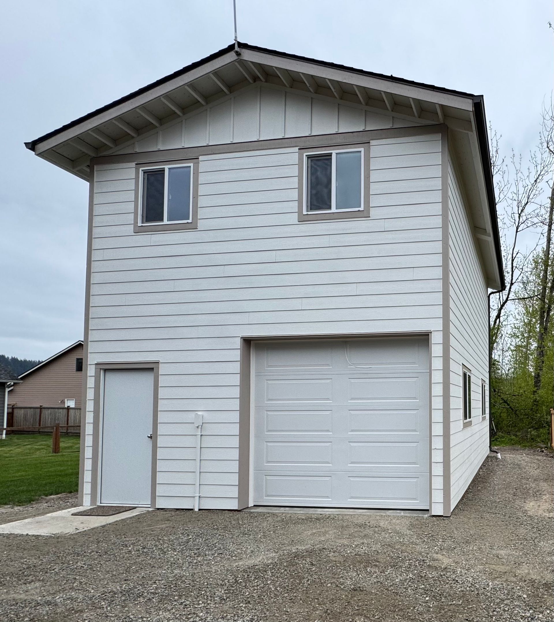 Two-story white garage with a door, a garage door, and two upstairs windows. Gravel driveway.