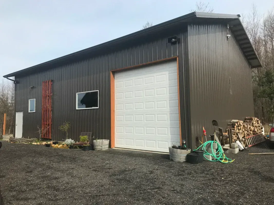 Brown metal shed with white garage door, small windows, and woodpile.