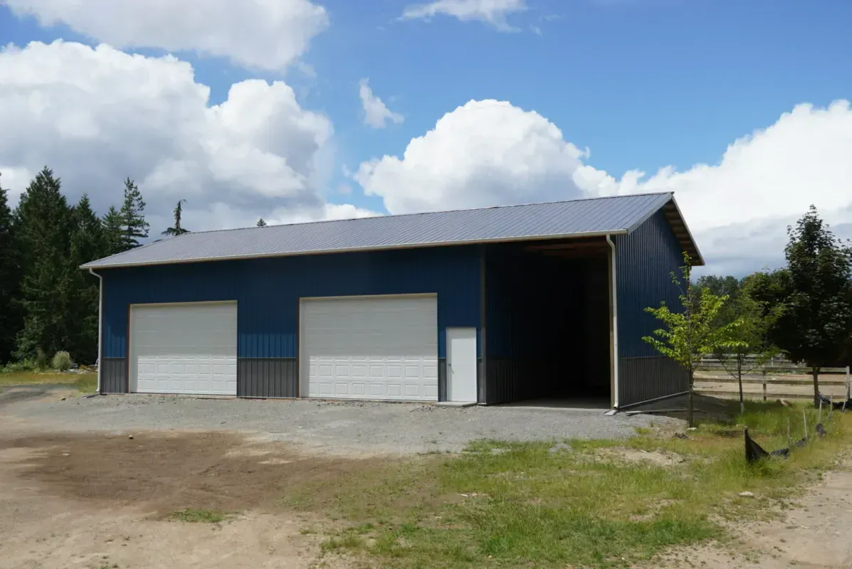 Blue and grey barn with two garage doors and open side; sunny day with clouds.