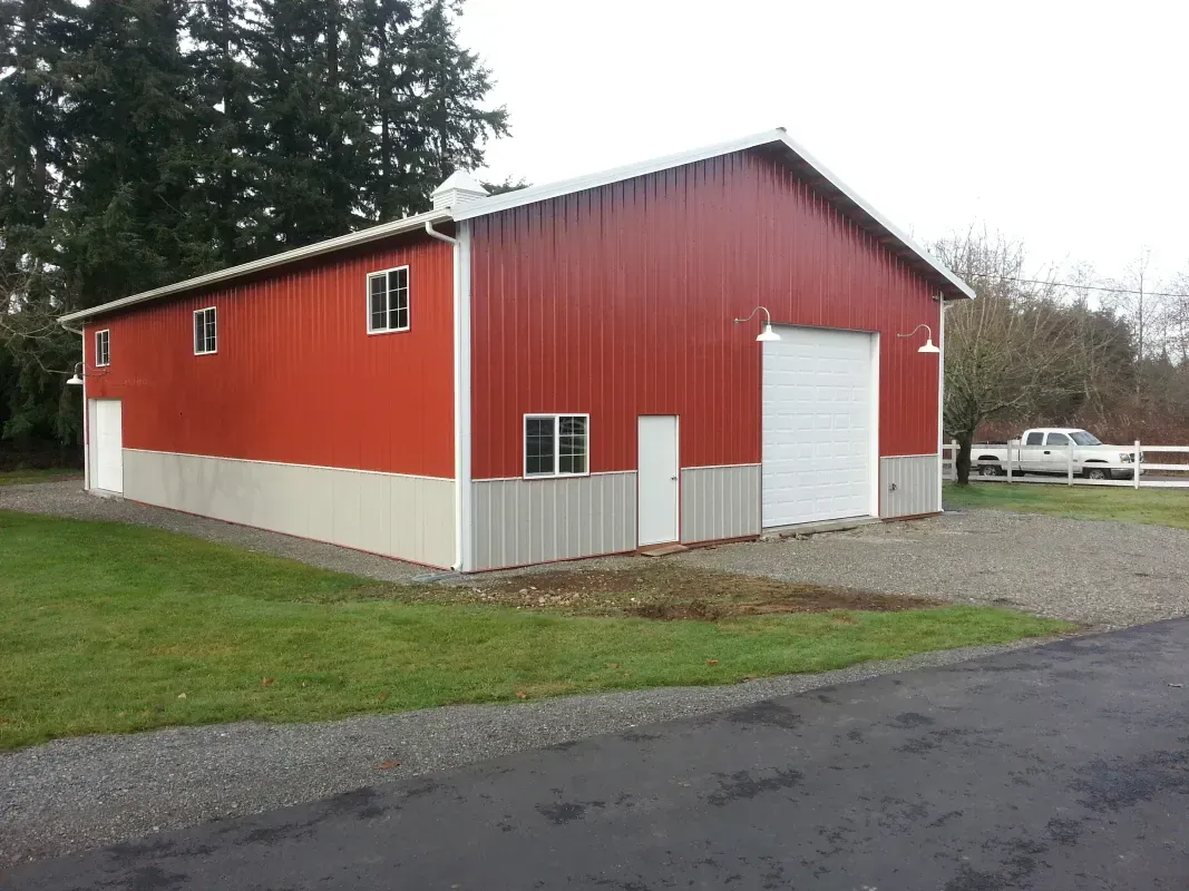 Red and gray barn with white trim, gravel driveway, and a truck parked nearby.