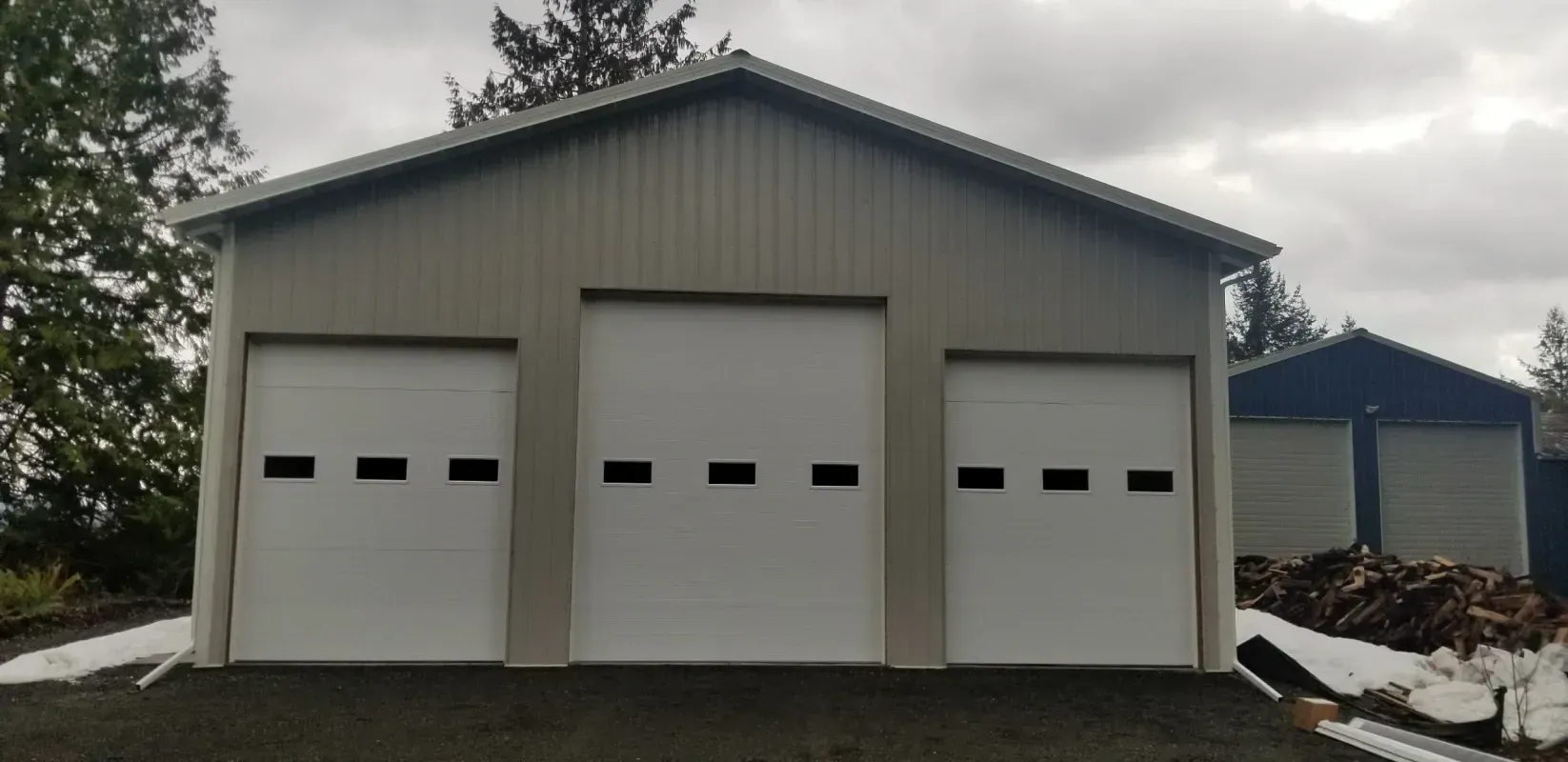 A three-bay garage with white garage doors sits under a cloudy sky.