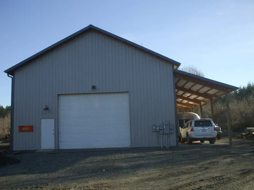 Metal garage with a carport; a white car is parked under the carport.