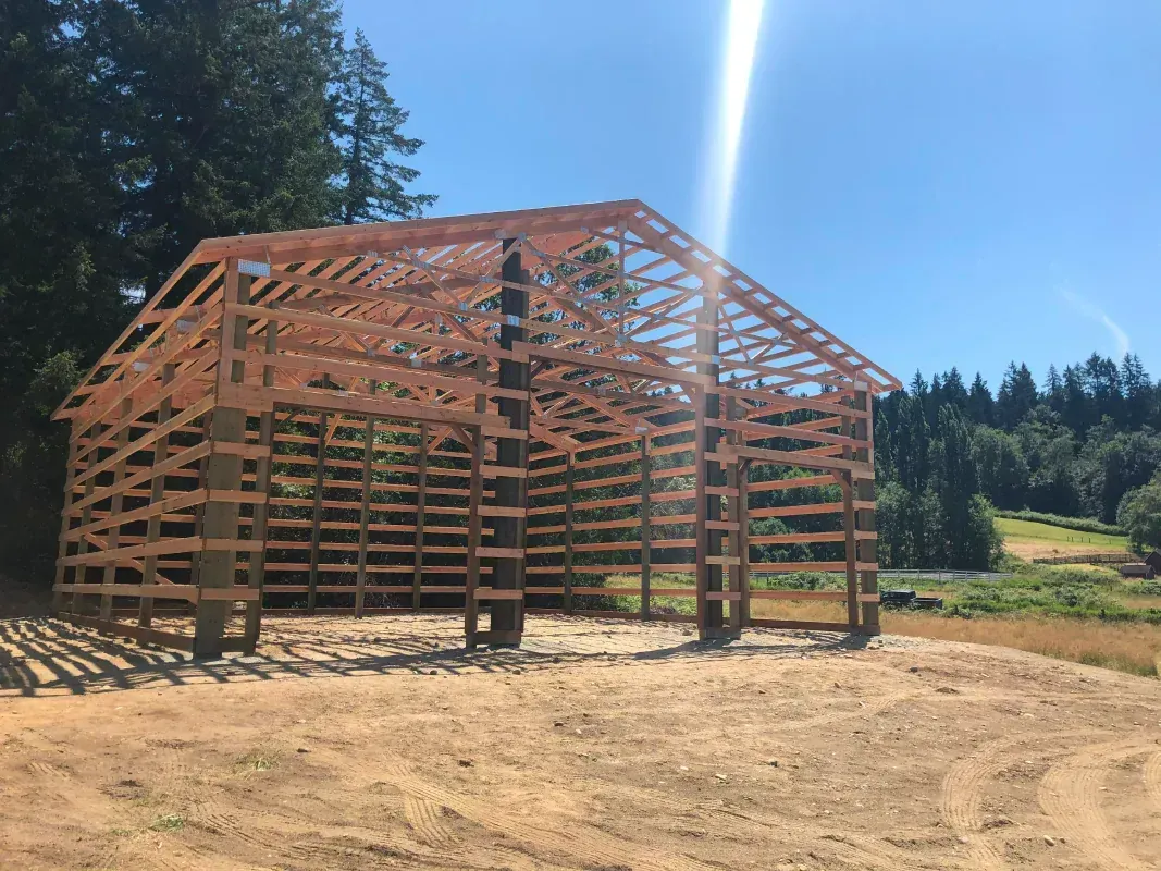 Wooden barn frame under construction on a sunny day.