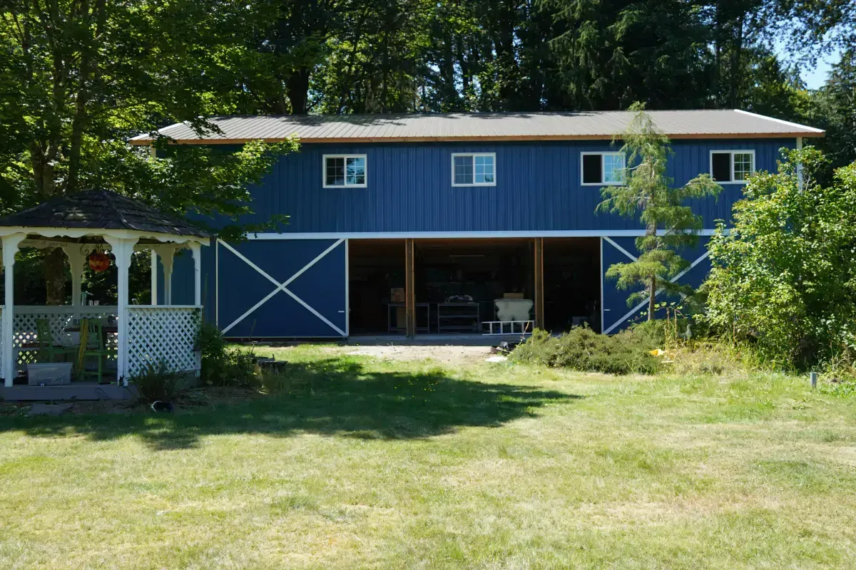 Blue barn with white accents, open doors revealing interior, next to a white gazebo.