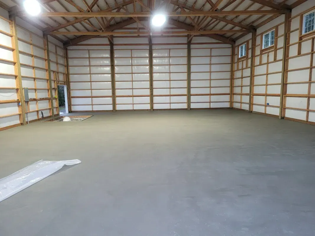 Empty concrete interior of a large wooden structure with white walls and windows.