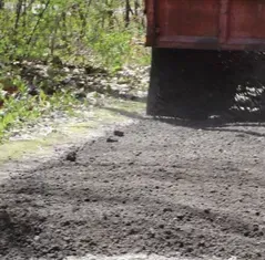 A red dump truck is driving down a dirt road.