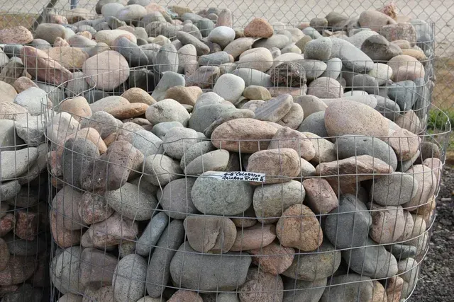 A pile of fieldstone rocks sitting on top of a wire fence.