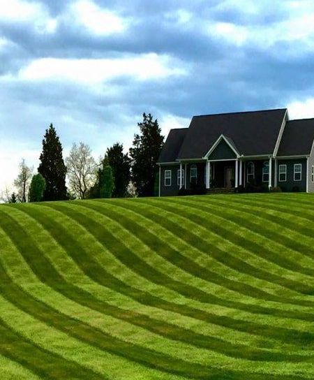 A house is sitting on top of a hill with a lush green lawn in front of it.