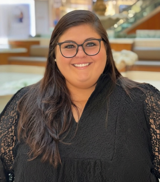 Woman in black dress and man in a suit pose together, smiling, near a bar.