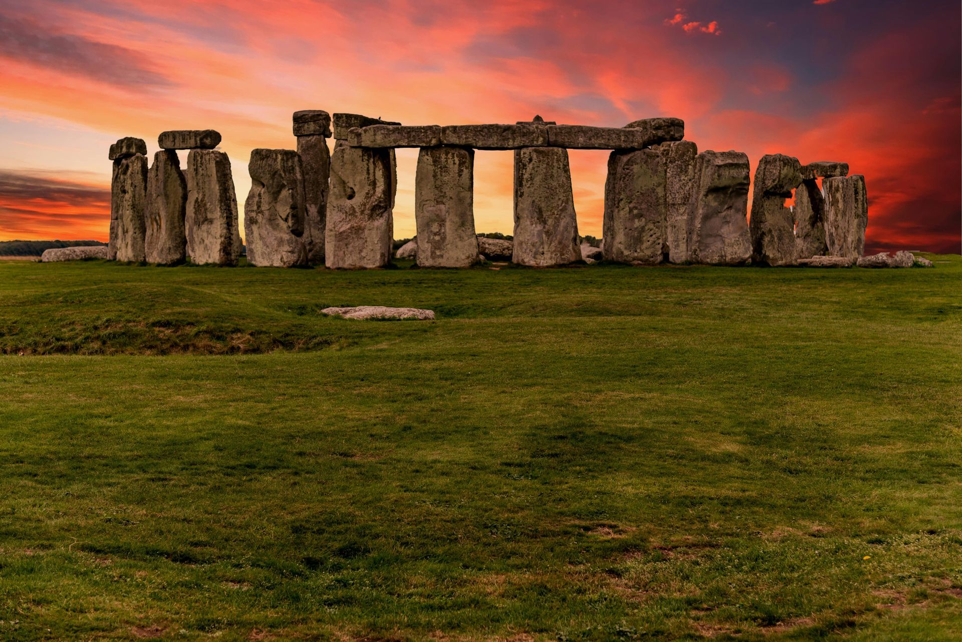 Stonehenge, prehistoric monument in a green field with a colorful sunset sky.