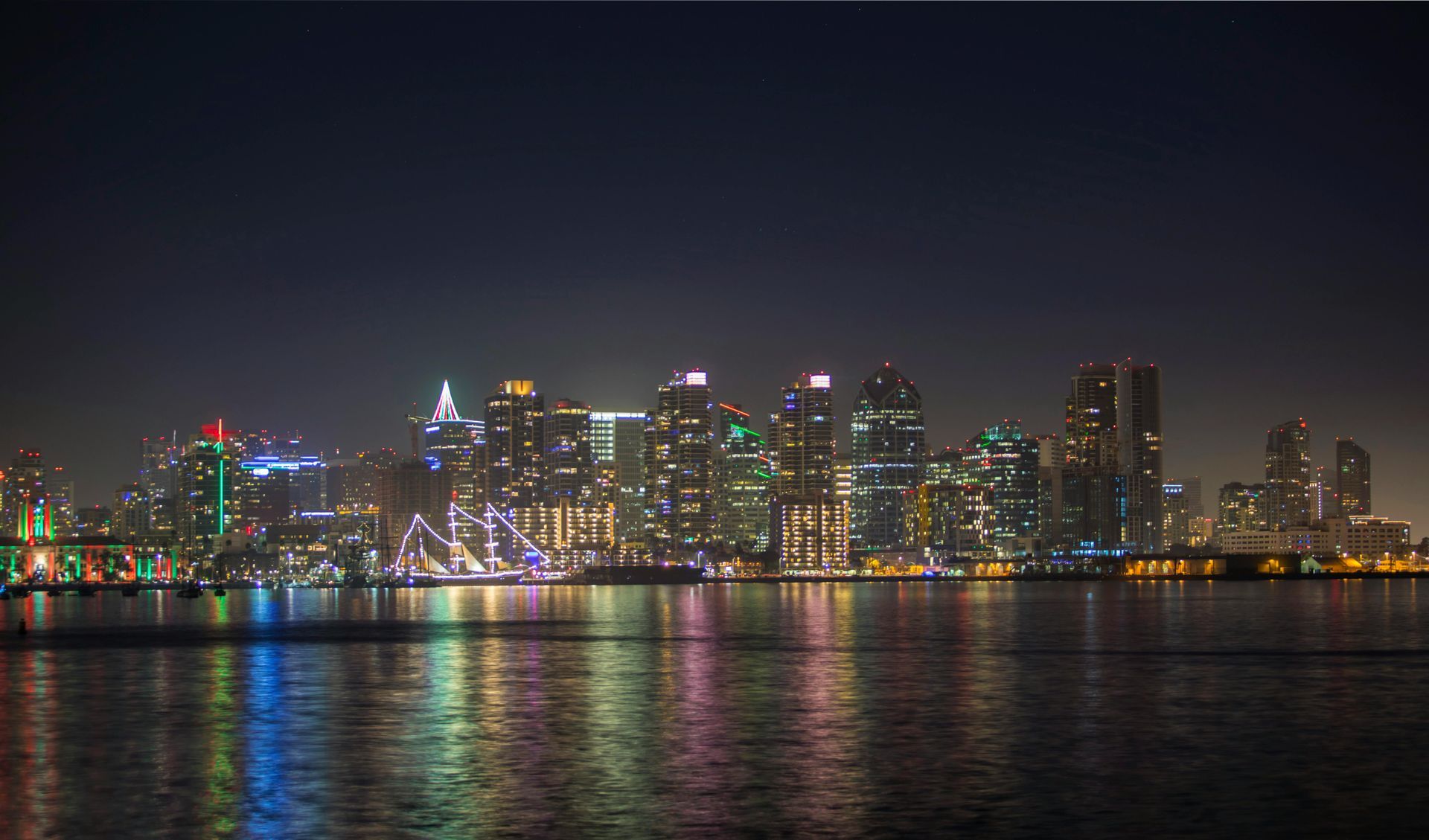 Nighttime cityscape with glowing buildings reflected in dark water.