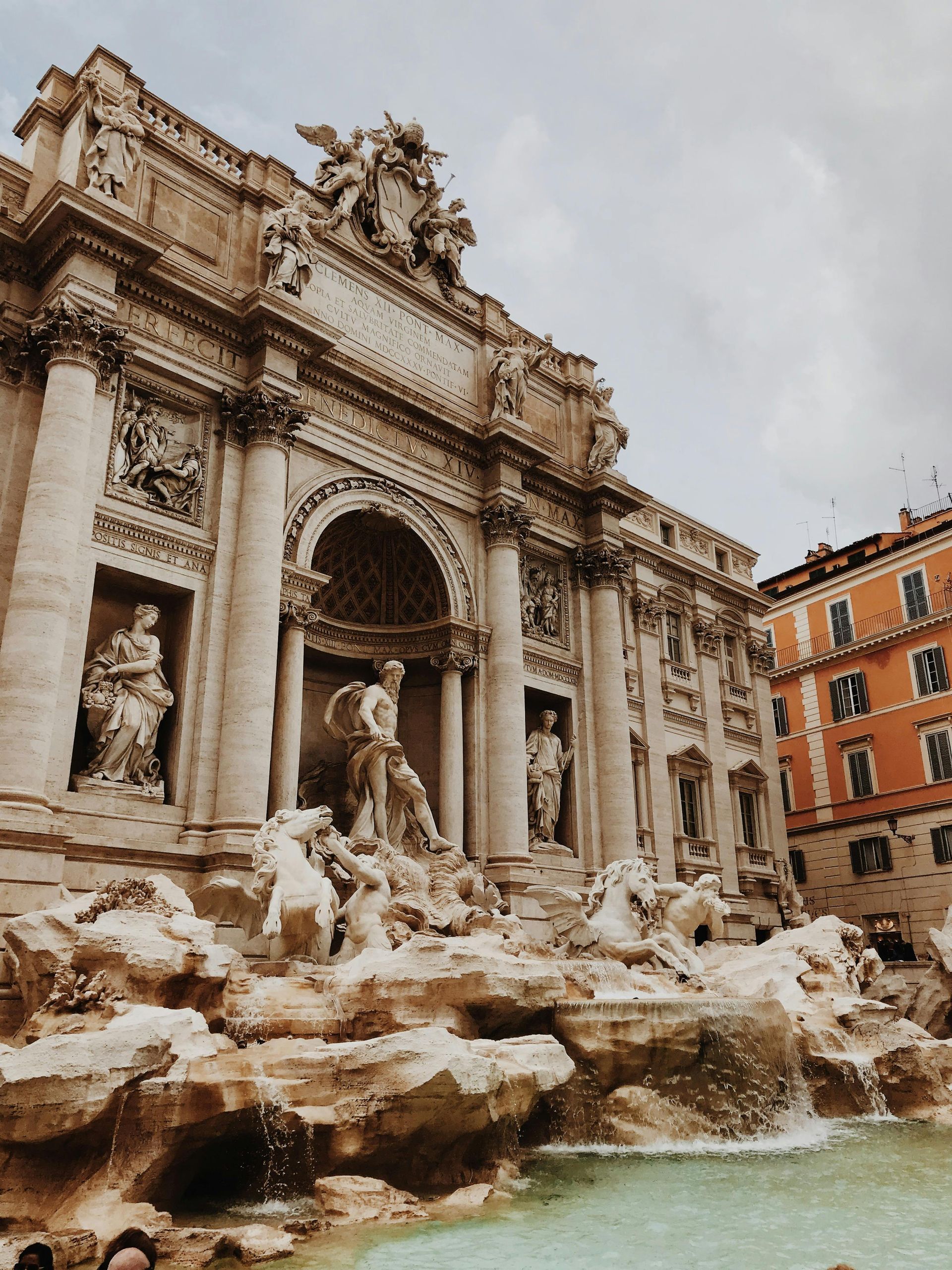 Trevi Fountain, Rome. Baroque architecture with sculptures, water flowing into a large basin, and an orange building to the right.