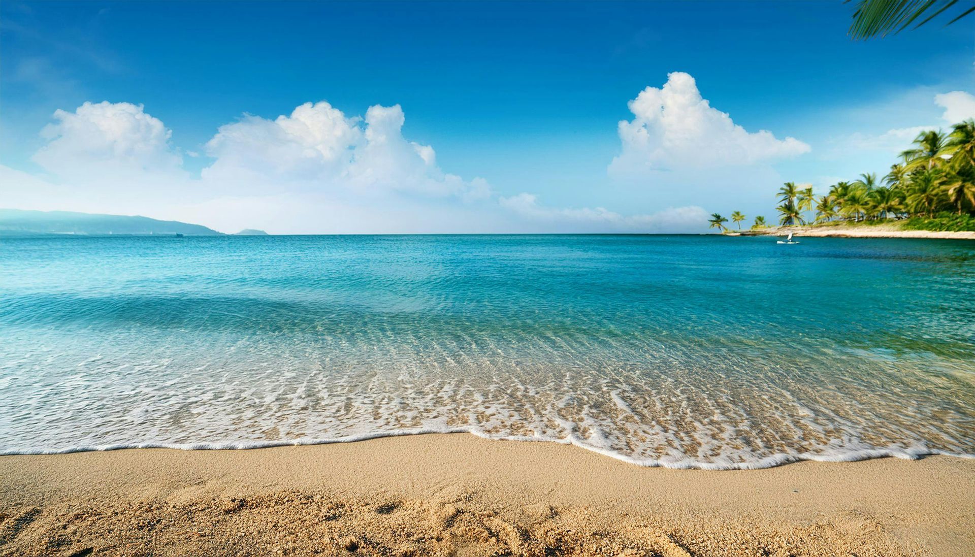 Sandy beach with clear turquoise water and blue sky with clouds.