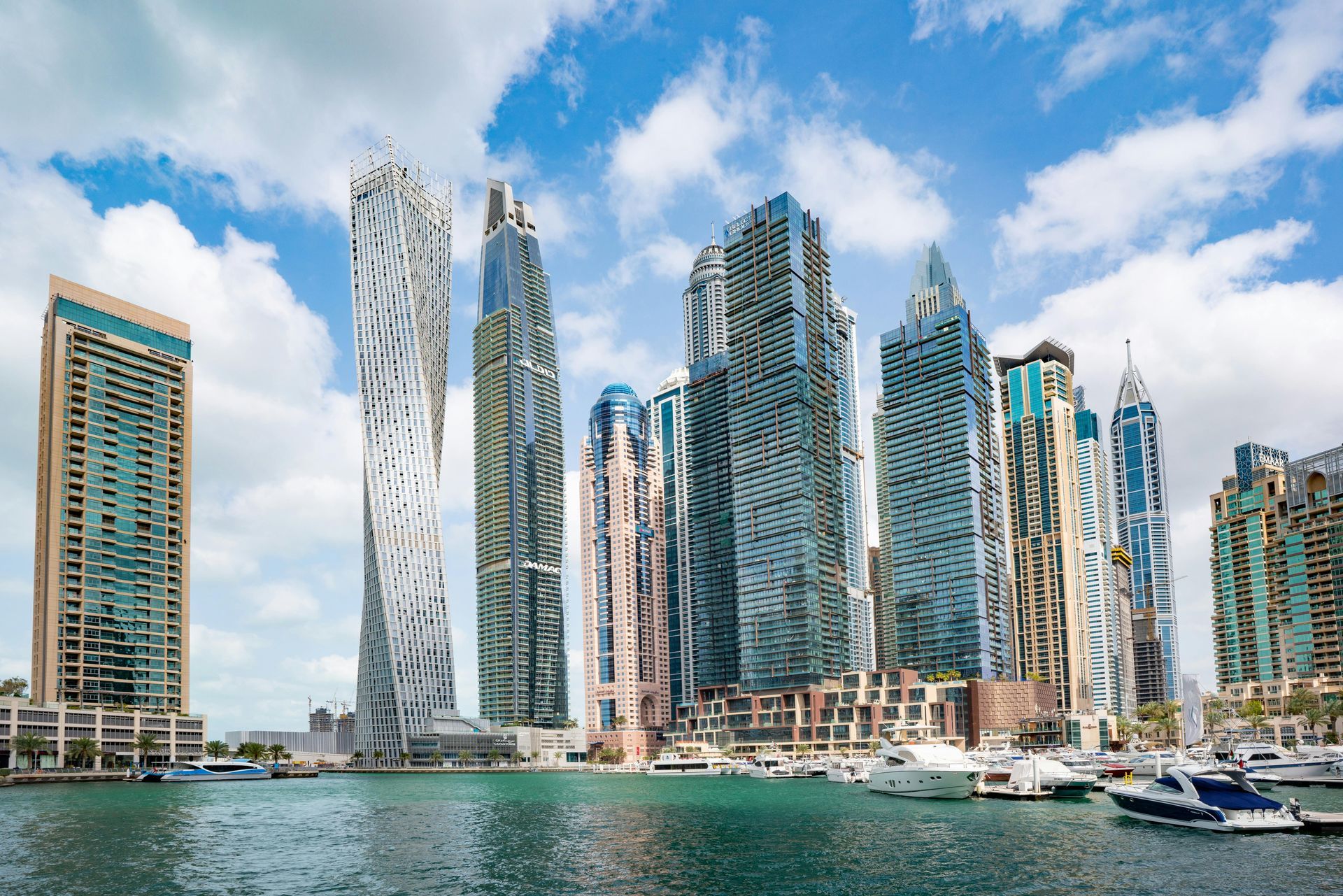 Dubai skyline, with modern skyscrapers along a marina, blue sky and scattered clouds.