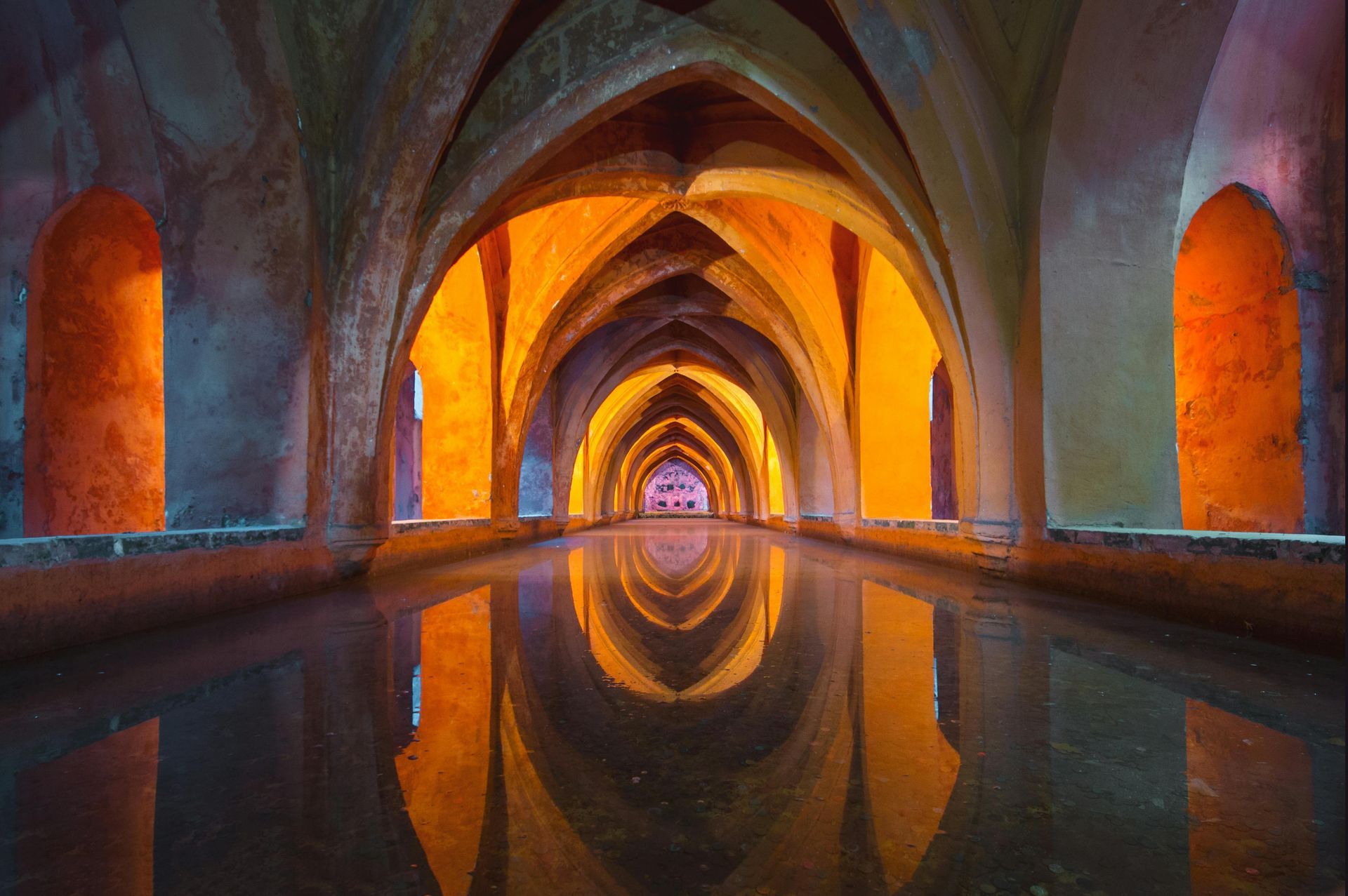Arched water cistern with warm light illuminating the interior; the arches are reflected in the water.