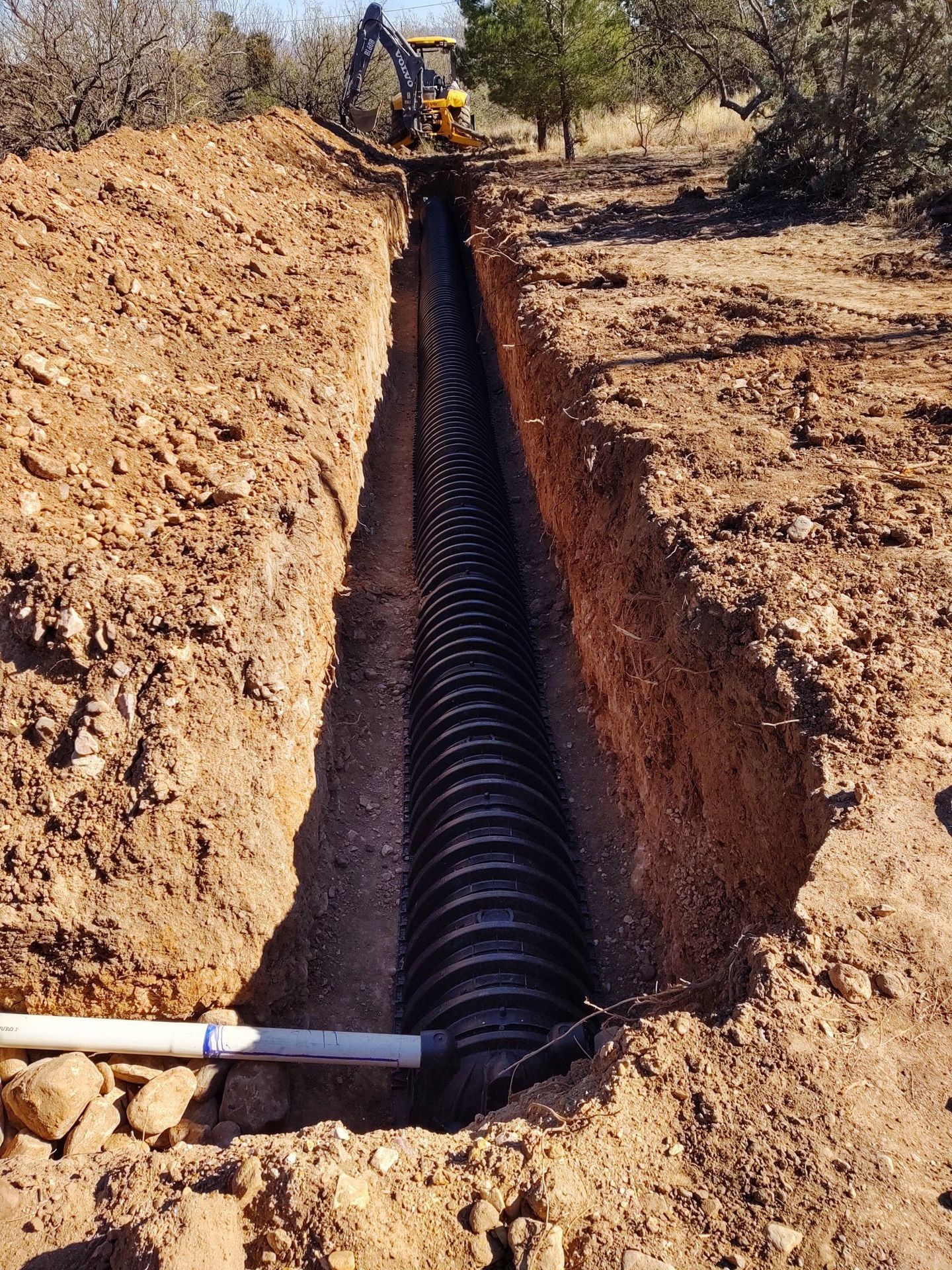 A large pipe is being installed in a trench in the dirt