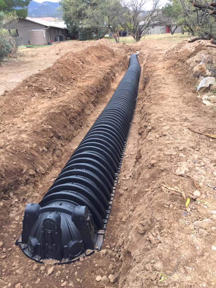 A large black pipe is sitting in the middle of a dirt field