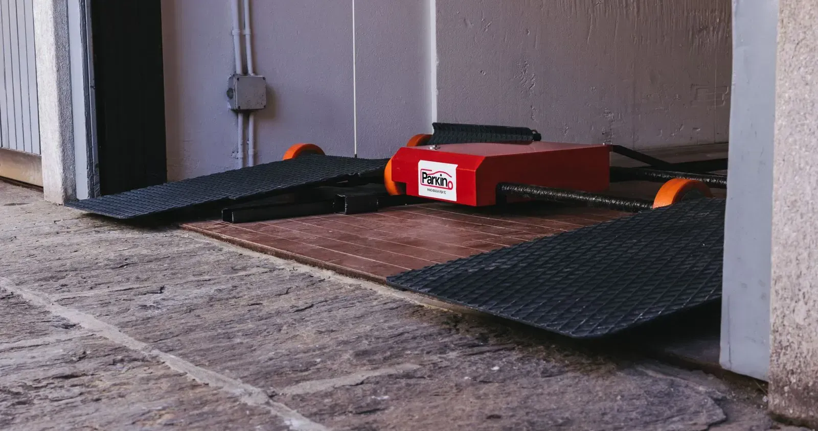 Un uomo con un casco giallo sorride, tenendo in mano un blocco per appunti vicino a una telecamera di sicurezza e a un trapano.