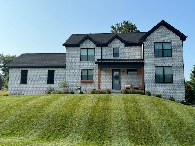 A large white brick house sits on top of a lush green hillside.