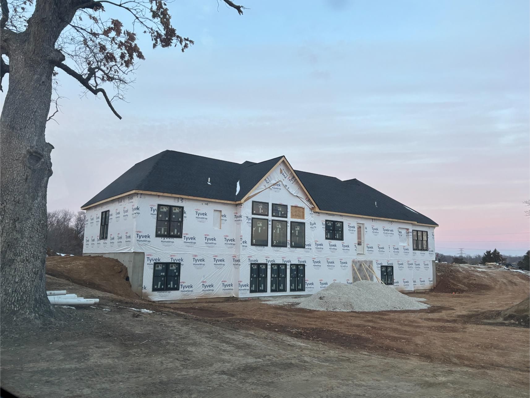 House under construction, covered in white wrap, dark roof, windows, exterior setting.