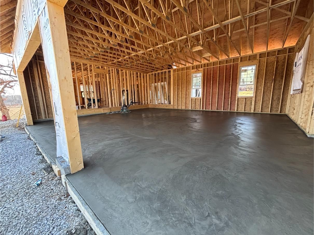 Interior view of a new garage under construction with a freshly poured concrete floor and exposed wooden framing.