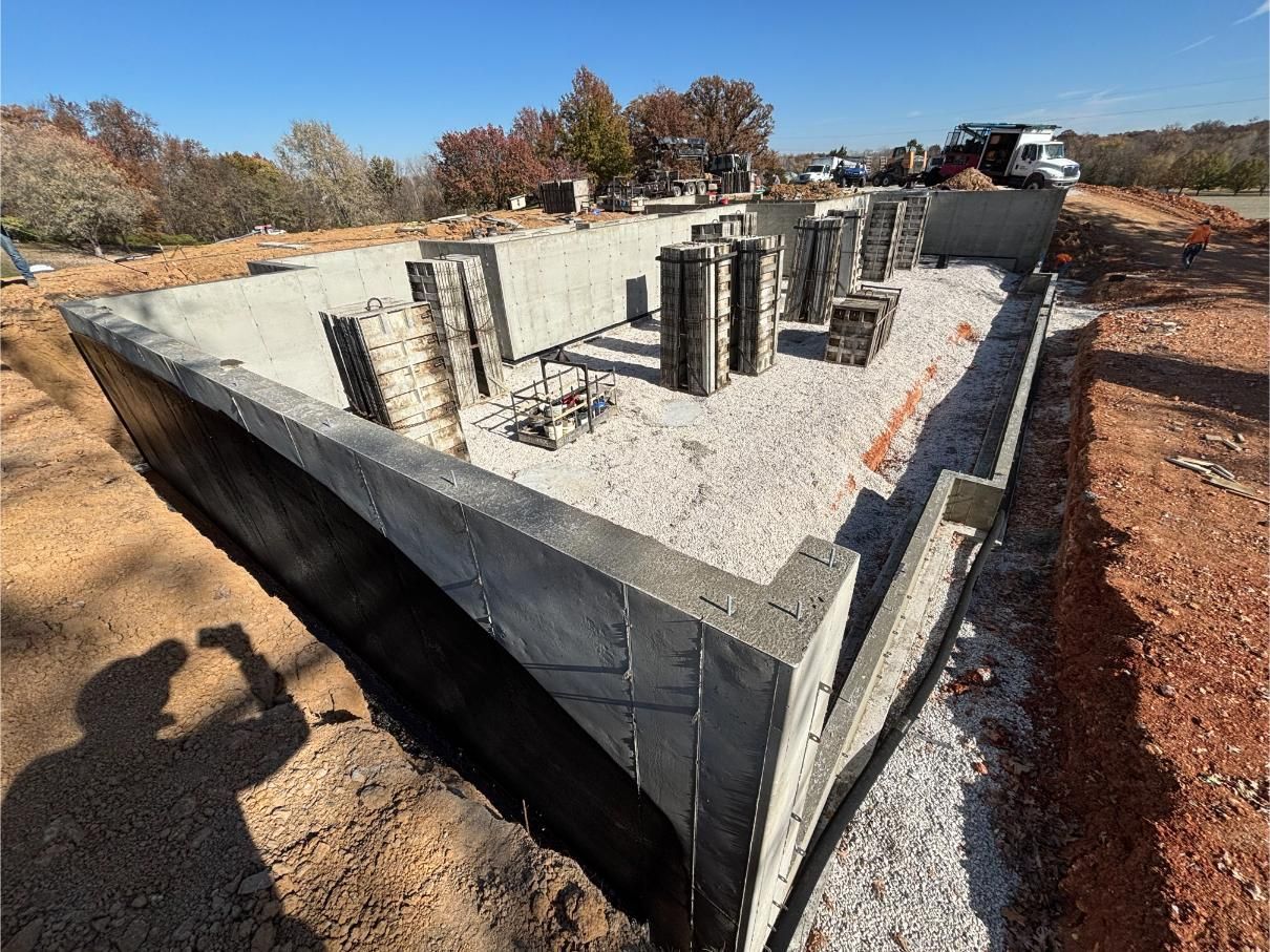 Concrete foundation being built, gravel base, rebar, and partially completed walls on a construction site.