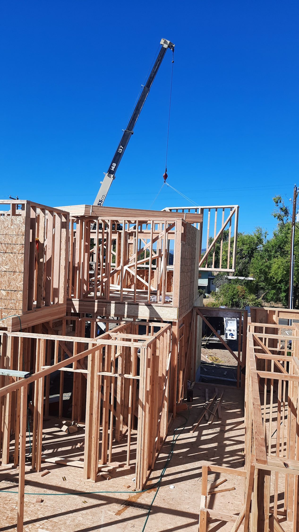 Construction site with wooden frame structure and crane against a blue sky.