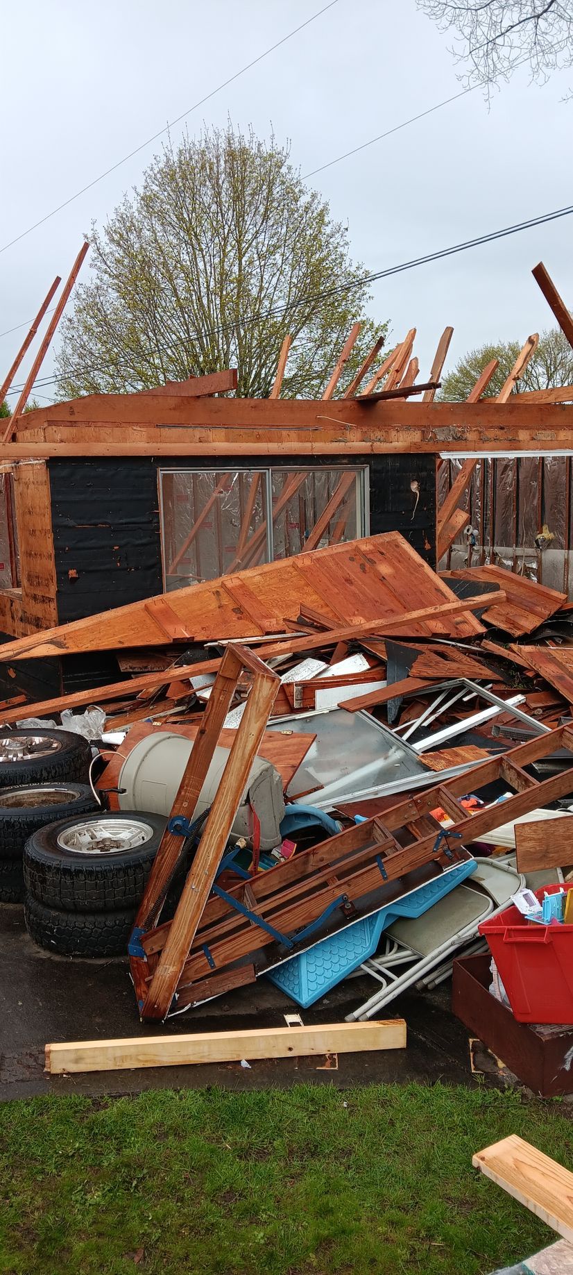 Debris from a demolished building, including tires, wood, and metal, scattered in a yard.