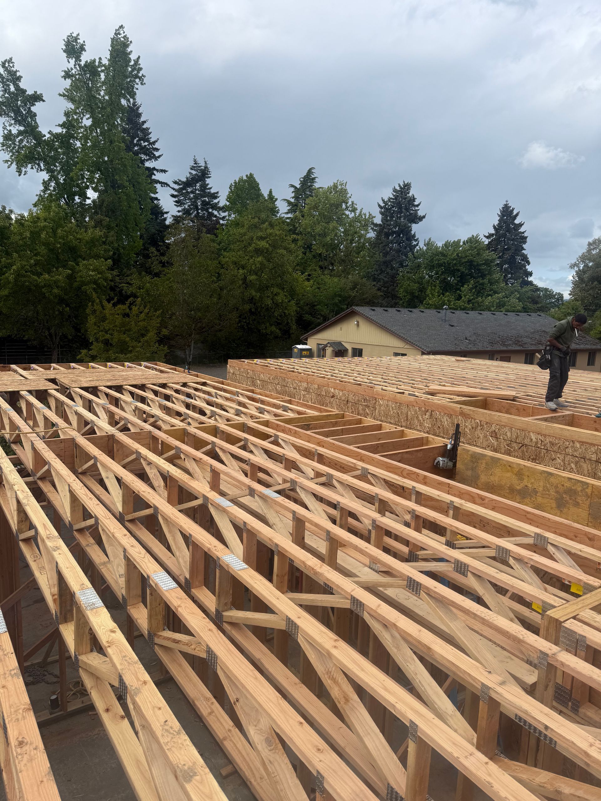 Wooden roof trusses being installed on a structure, with trees and a house in the background.