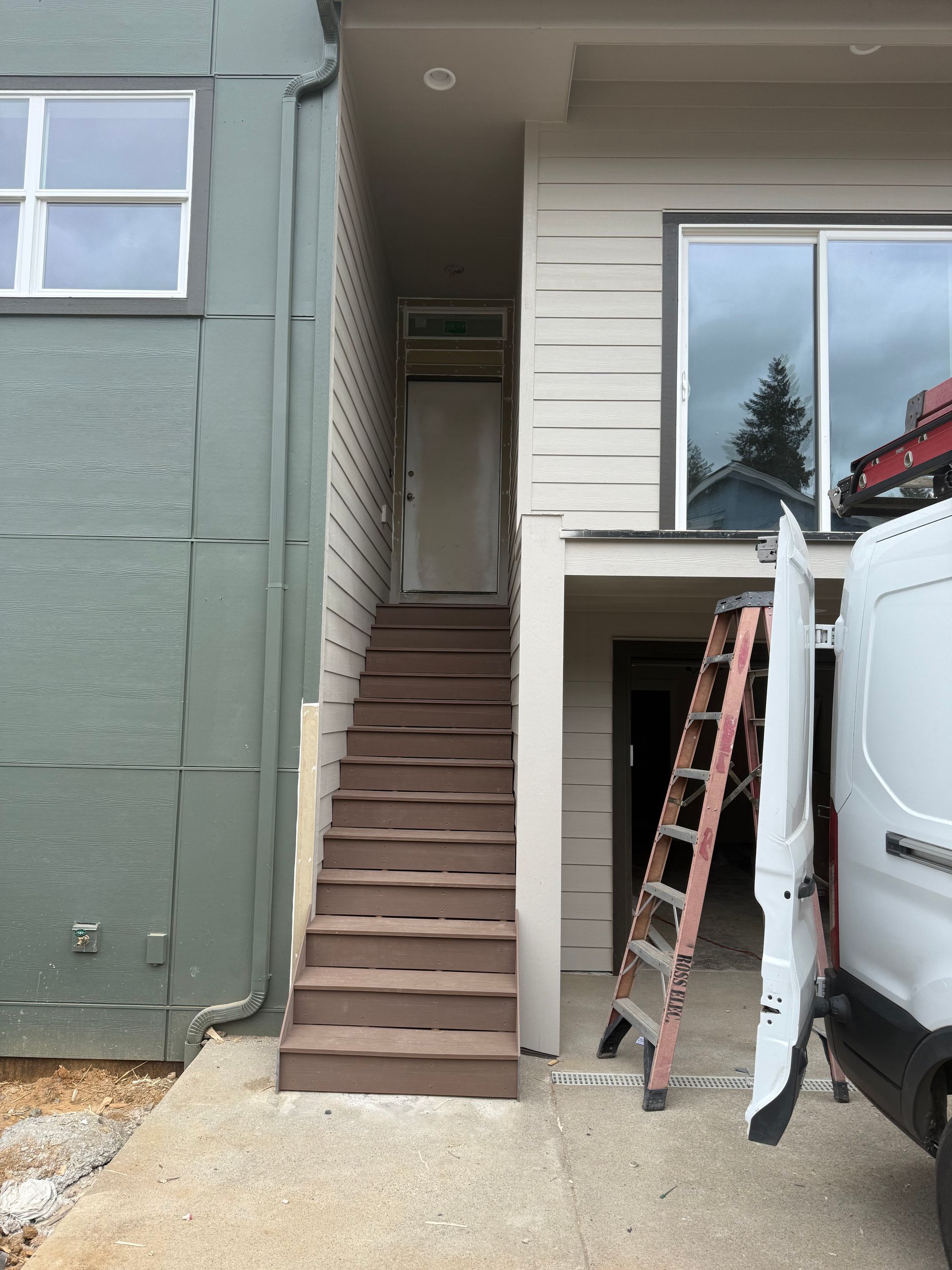 Outdoor stairs leading to a door between two buildings. A ladder and van are nearby.