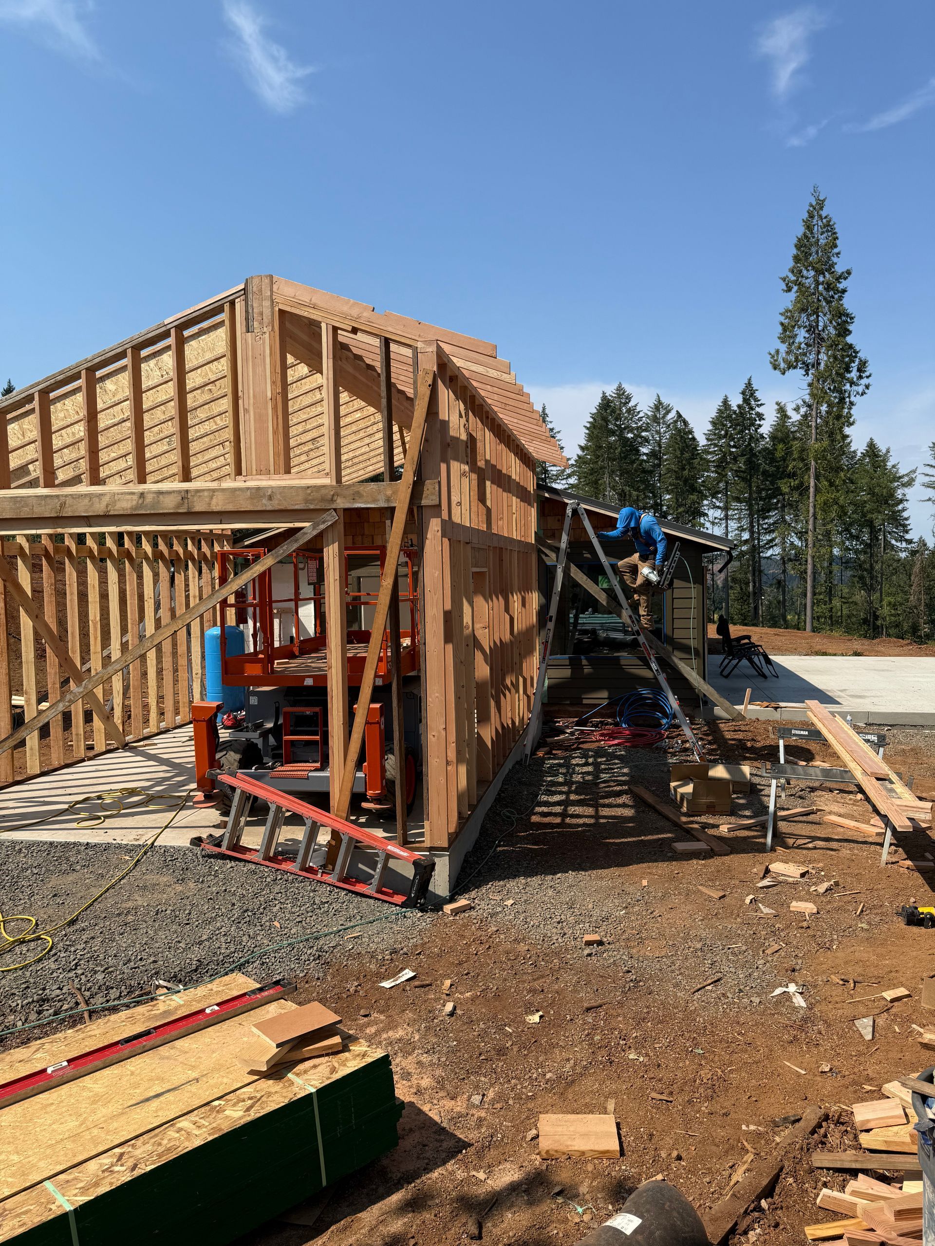 Construction site, wooden framing of a building in progress under a blue sky. Lumber and equipment visible.