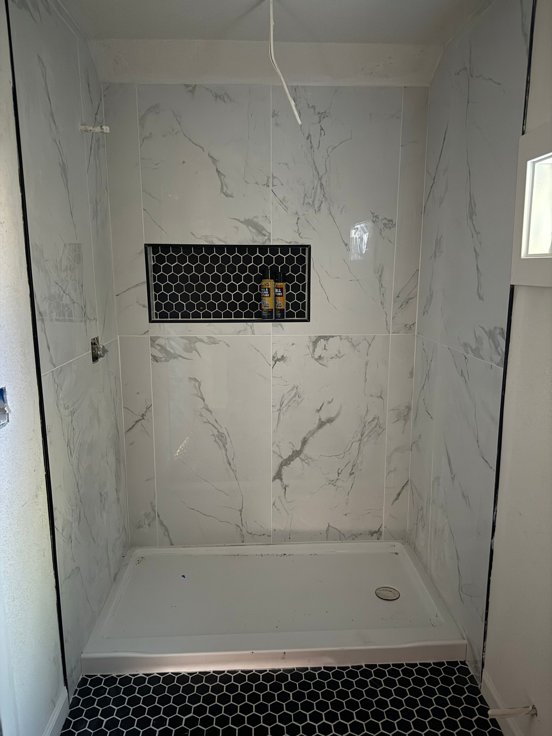 Newly tiled shower with white marble-like walls, black mosaic floor, and a black accent niche.