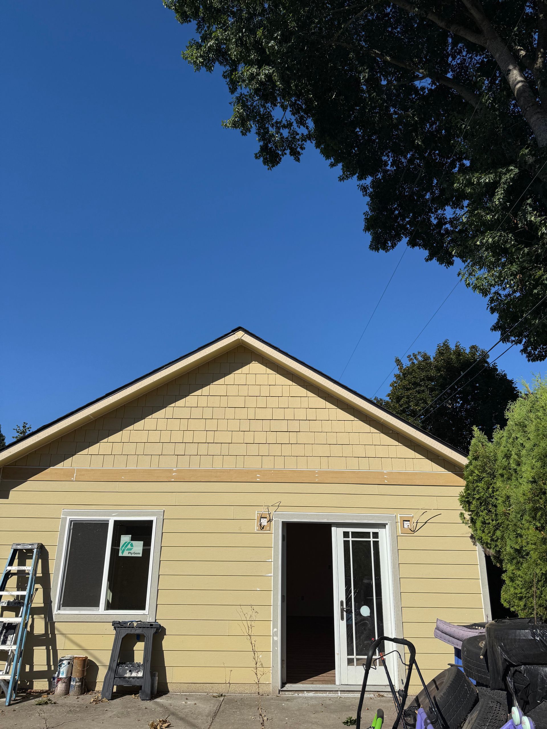 A yellow-sided building under construction with a sliding door and window against a blue sky.