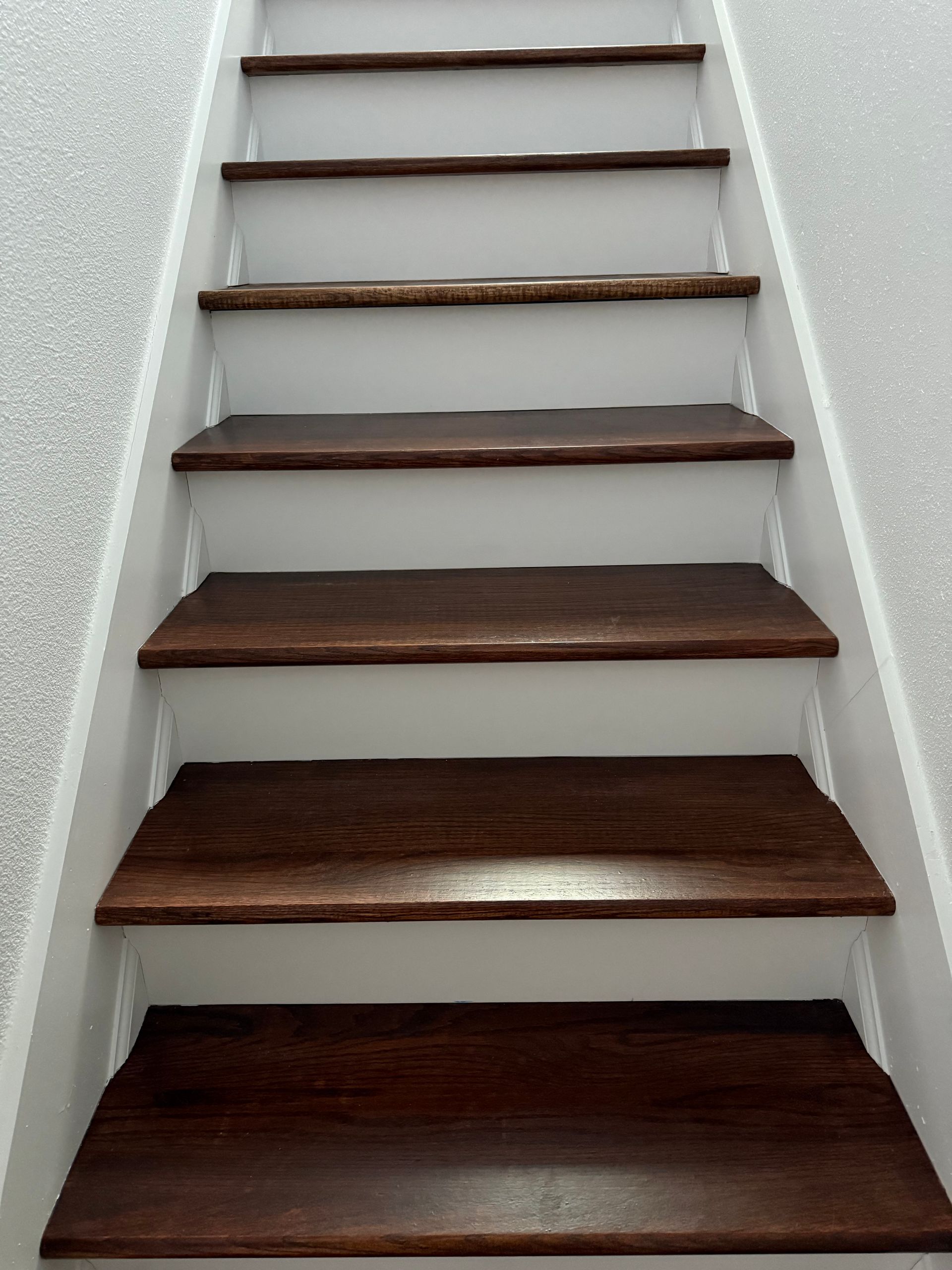 Wooden stairs with dark treads and white risers, ascending in a home with gray walls.