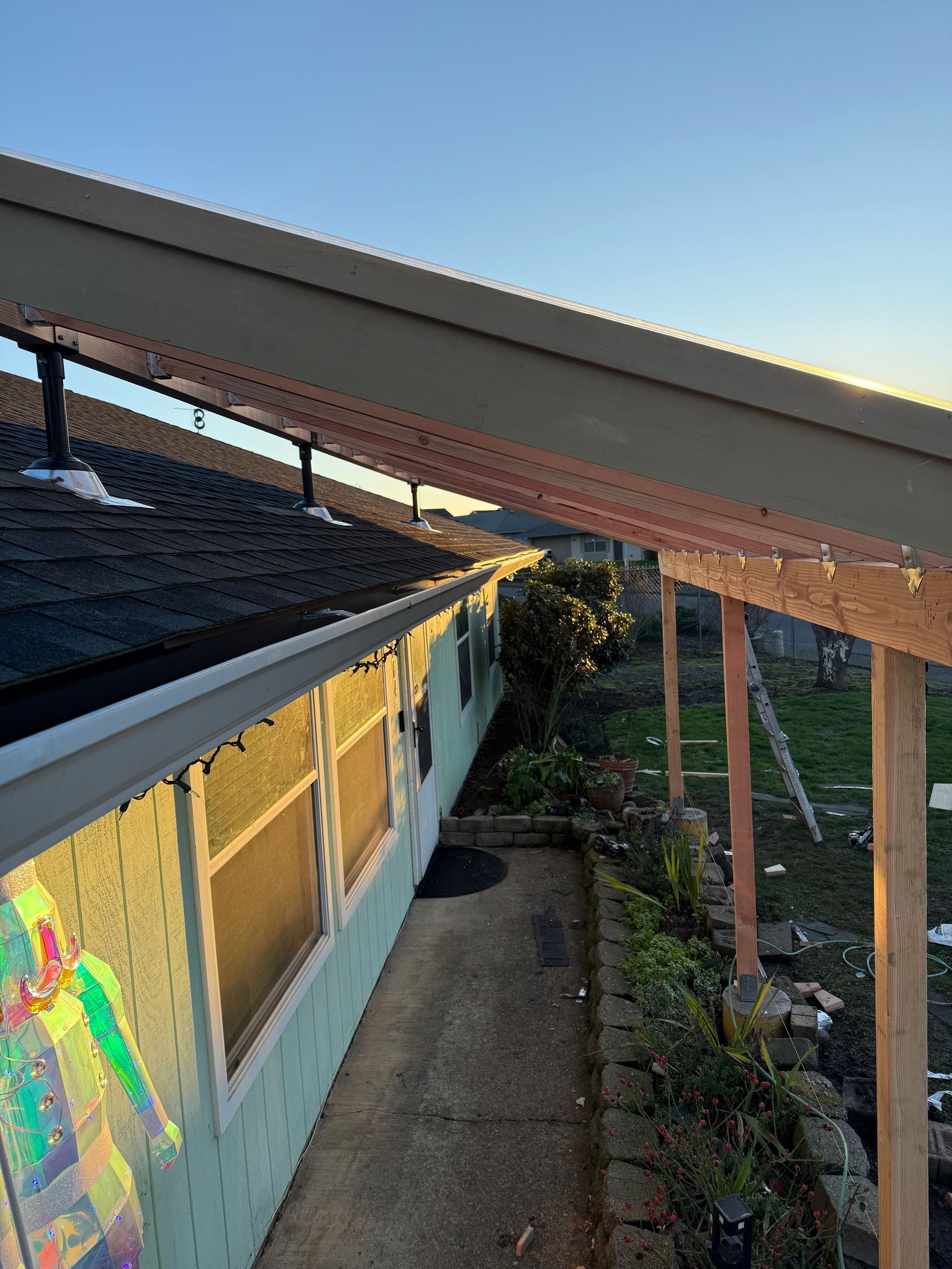 View of a house's roof, gutter, and porch with the blue sky in the background, lit by the golden sun.