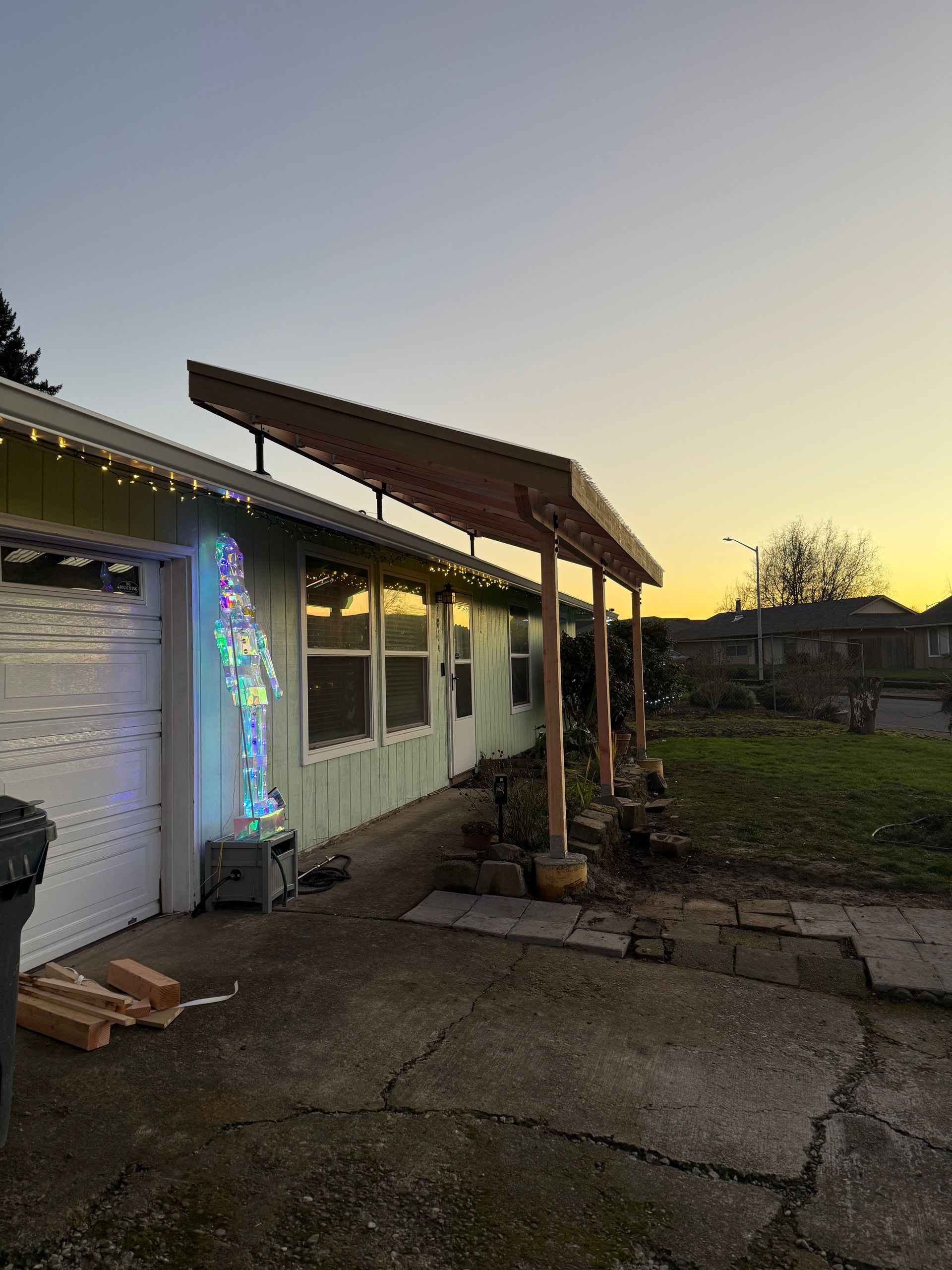 A house with a slanted wooden awning. Colorful Christmas lights are displayed. Dusk with golden hues.