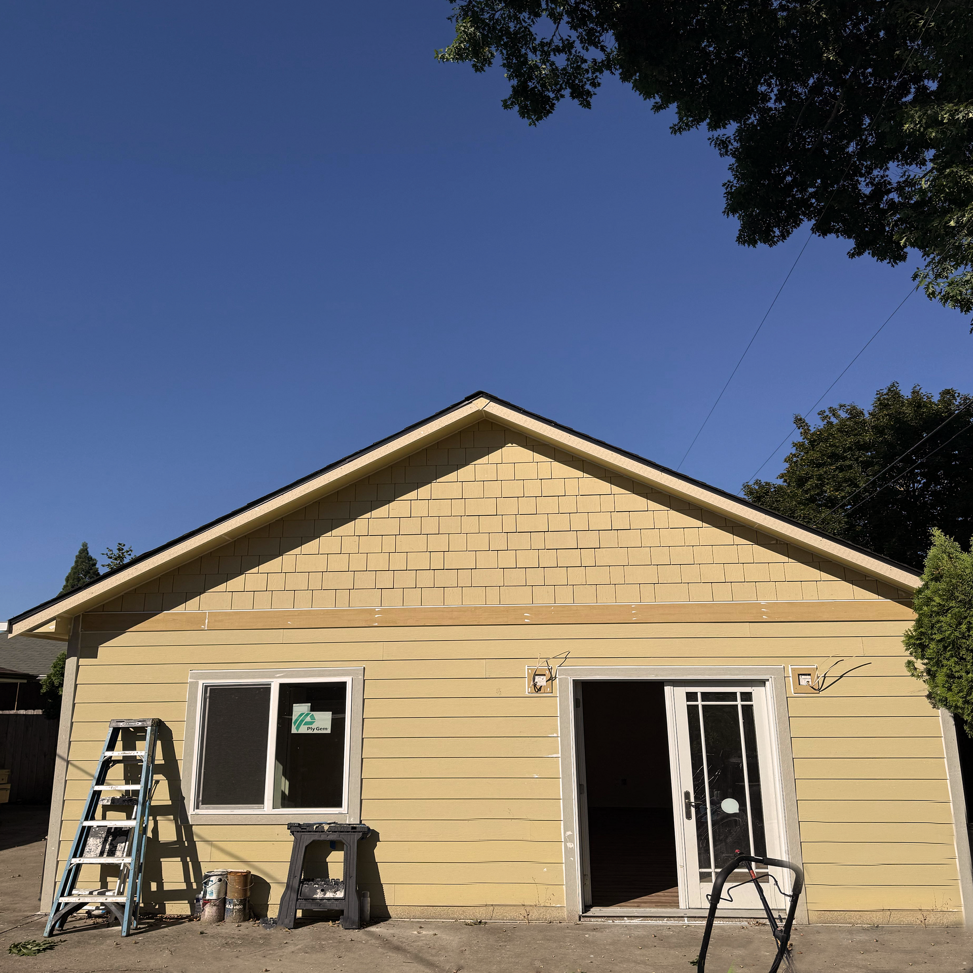 Yellow house under construction with ladder, open sliding door, and clear blue sky.