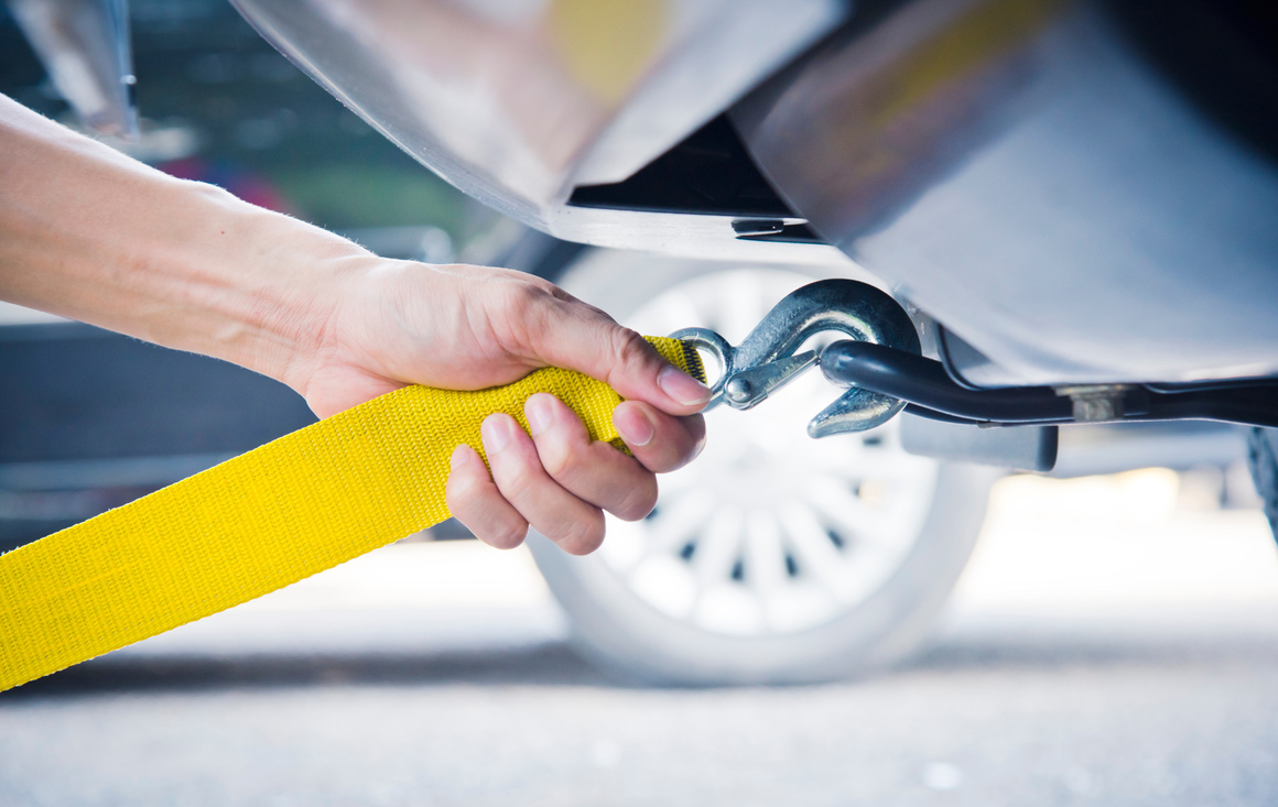 A person is towing a car with a yellow tow strap.