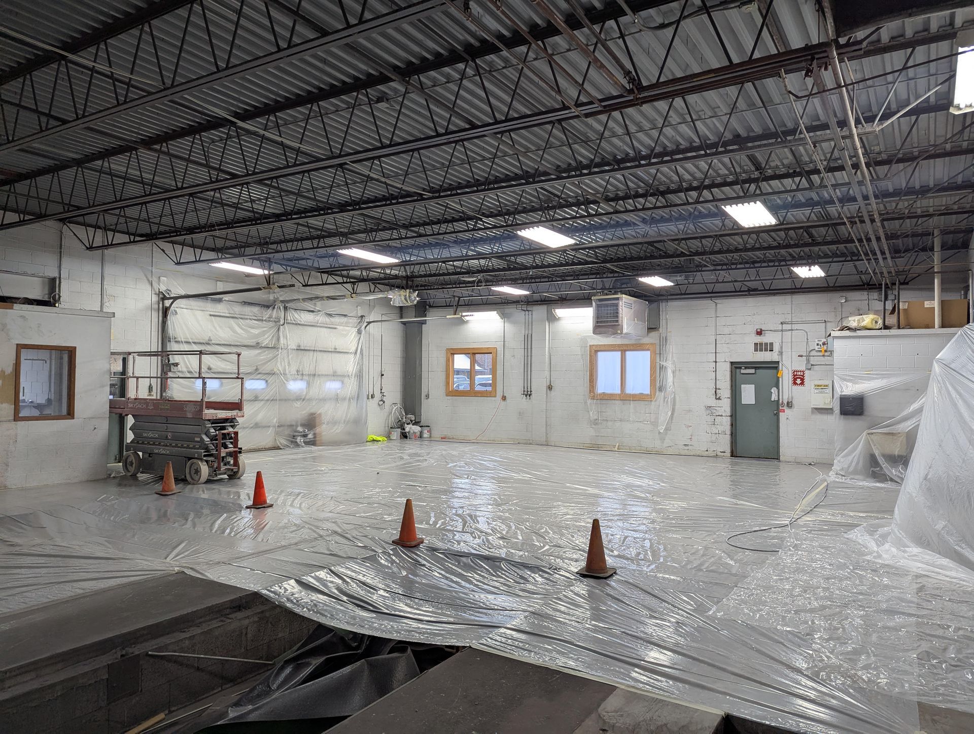 Interior view of an empty warehouse space, covered in plastic sheeting, with construction equipment visible.