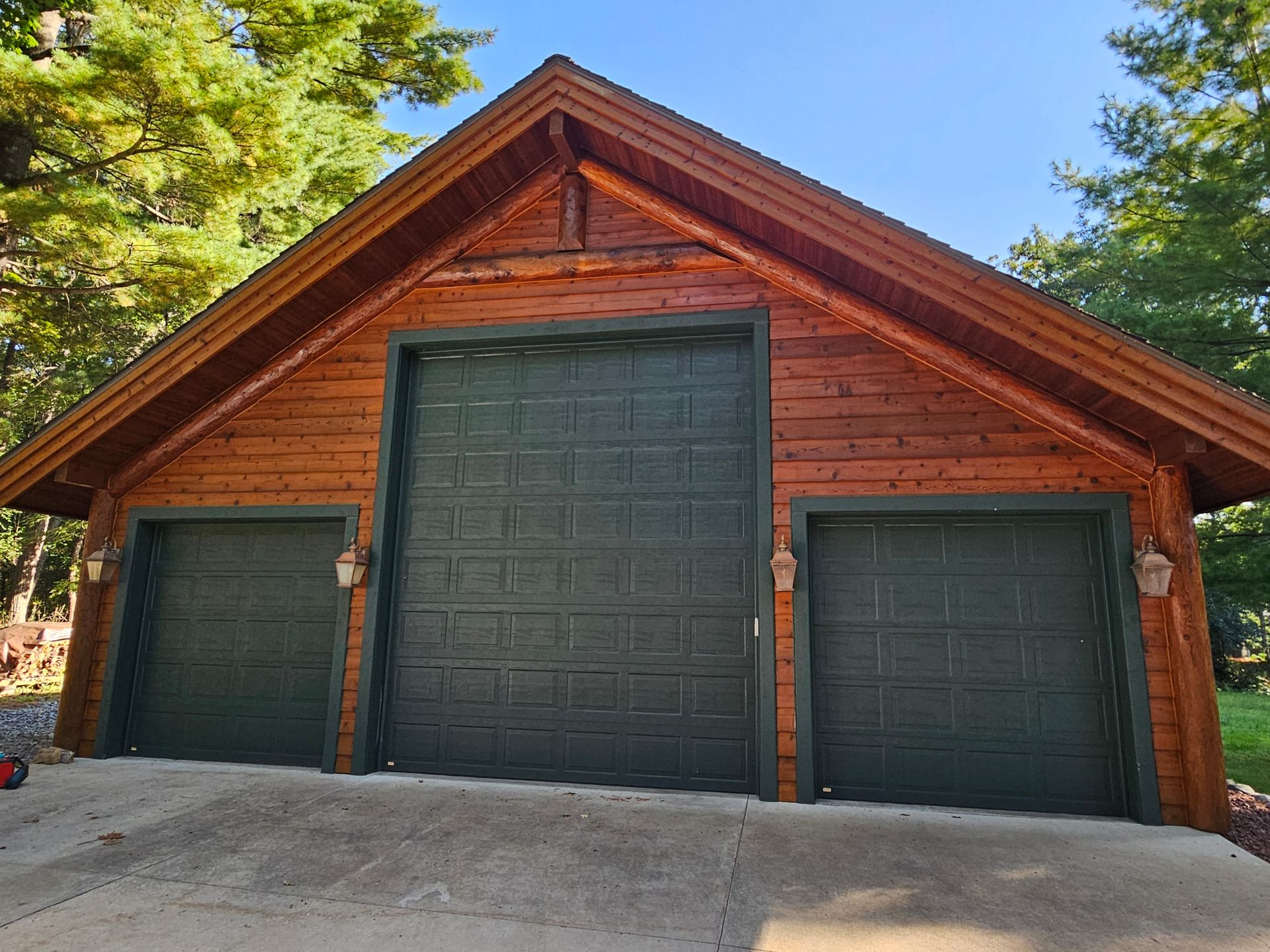 Wooden garage with three dark green garage doors under a triangular roof.